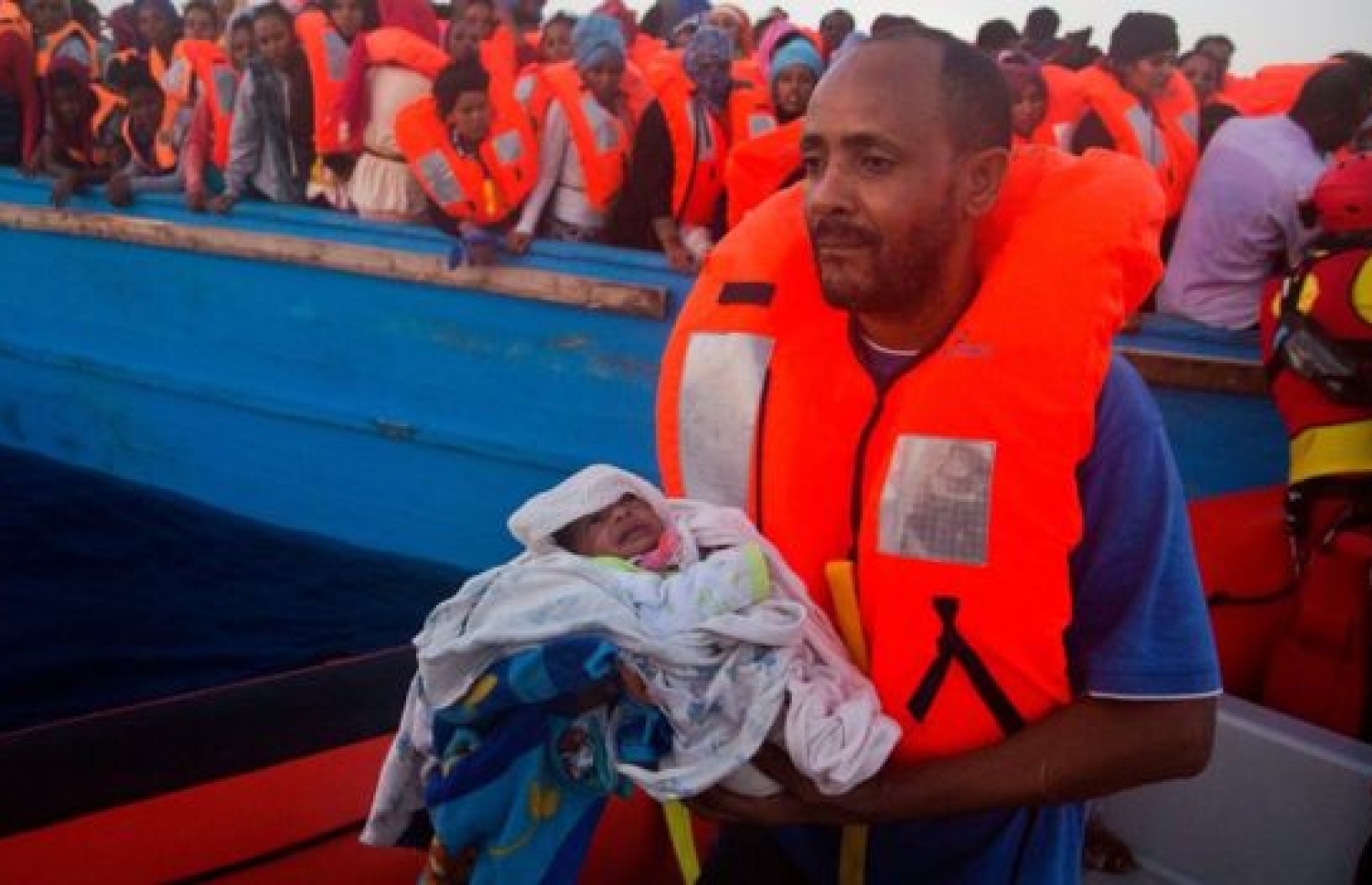 ރެފިއުޖީން ތިބި ބޯޓަކުން ފަސް ދުވަސްވީ ކުޑަ ކުއްޖަކު ގޮވައިގެން ރެސްކިއު ބޯޓަކަށް މީހަކު ދަނީ. --ފޮޓޯ:އޭއެފްޕީ