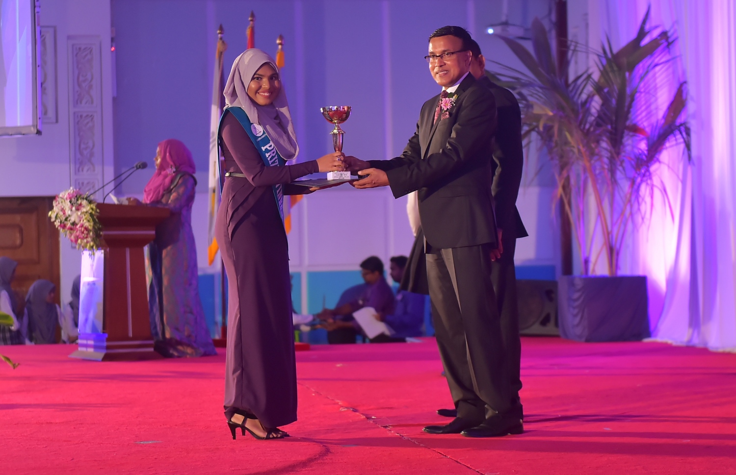 މާލެ: އޮކްޓޯބަރު 8، 2016- އަހުމަދިއްޔާ އިންޓަނޭޝަނަލް ސްކޫލުގެ އިނާމު ދިނުމަށް ބޭއްވި ޖަލްސާގެ ޝަރަފުވެރި މެހުމާން އެޑިއުކޭޝަން މިނިސްޓްރީގެ ސްޓޭޓް މިނިސްޓަރު ޑރ. އަބްދުﷲ ނަޒީރު އިނާމު ހަވާލުކޮށްދެއްވަނީ: އެ ސްކޫލުން މިދިޔަ އަހަރު ސެކަންޑަރީ ބައިން އެއްވަނަ ހޯދީ ފާތިމަތު ނަޝާ އަލީ އަދި ހަޔަ ސެކަންޑްރީ ބައިގެ އެއްވަނަ ދަރިވަރަކީ އާމިނަތު ރިފްޒާ.---ފޮޓޯ: މުހައްމަދު ޝަރުހާން/މިހާރު