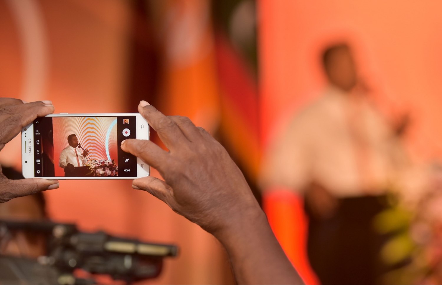 މާލެ: މާޗް 6، 2017- ލޯކަލް ކައުންސިލްތަކުގެ އިންތިޚާބުގައި އެމްޑީއޭ އިން ވާދަކުރާ ކެންޑިޑޭޓުން ތައާރަފު ކުރުމަށް ބޭއްވި ޖަލްސާގައި، ހޯރަފުށީ ދާއިރާގެ މެމްބަރު މުހައްމަދު އިސްމާއިލް ވާހަކަ ދައްކަވާއިރު، އޭނާގެ ފޮޓޯއެއް މޮބައިލް ފޯނުން މީހަކު ނަގަނީ.---ފޮޓޯ: ހުސެއިން ވަހީދު/މިހާރު