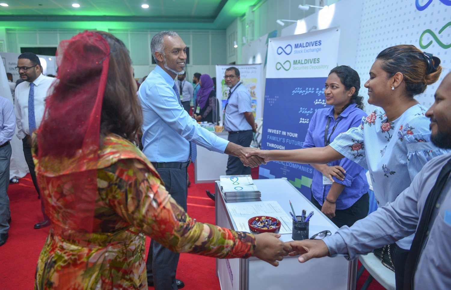 މާލެ: ޖުލައި 6، 2017- ގެދޮރުވެރިކަމަށް ބޭނުންވާ ފައިސާ ހޯދޭނެ ގޮތްތަކާ ބެހޭ ގޮތުން އެމްއެމްއޭ އާއި އެޗްޑީސީ ގުޅިގެން ދަރުބާރުގޭގައި ފެށި މި އަހަރުގެ މޯލްޑިވްސް ފައިނޭންޝަލް އެކްސްޕޯގައި ހުރި މޯލްޑިވްސް ސްޓޮކް އެކްސްޗޭންޖުގެ ސްޓޯލެއްގައި ތިބި ދެ މުވައްޒަފަކާ، ހައުސިން މިނިސްޓަރު މުއިއްޒާއި އެމްއެމްއޭގެ ގަވަރުނަރު އަޒީމާ ސަލާމް ކުރައްވަނީ.---މިހާރު ފޮޓޯ: ހުސެއިން ވަހީދު