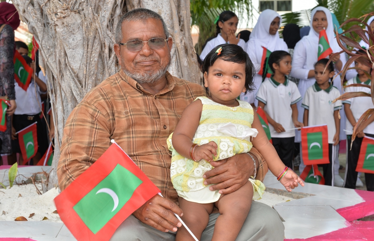 ގއ. ކޮލަމާފުށި: ސެޕްޓެމްބަރު 26، 2017- ރައީސް އަބްދުﷲ ޔާމީންގެ ދެކަނބަލުން ކޮލަމާފުއްޓަށް ވަޑައިގަންނަވާތީ އެ ދެކަނބަލުންނަށް މަރުހަބާ ދެންނެވުމަށް ތުއްތު ކުއްޖަކު ގޮވައިގެން ގޮސް ހުރި އުމުރުން ދުވަސްވީ މީހެއް..---ފޮޓޯ: ރައީސް އޮފީސް