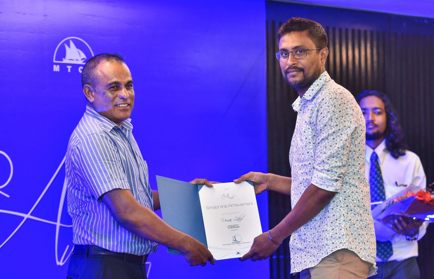 އޮކްޓޯބަރު 12، 2017- އެމްޓީސީސީގެ އެވޯޑް ނައިޓު ހަފުލާގައި، އެ ކުންފުނީގެ ސްކޮލަޝިޕް ލިބުނު މީހަކަށް އެކަމުގެ ލިޔުން ހަވާލު ކުރައްވަނީ: މި ހަފުލާގައި ވަނީ އެމްޓީސީސީ އަށް ދިގު މުއްދަތަކަށް ޚިދުމަތް ކުރި މުވައްޒަފުންގެ އިތުރުން އެ ކުންފުނިން ރިޓަޔާ ކުރި މުވައްޒަފުންގެ އަގުވަޒަން ކުރުމާ އެކު ހިއުމަން ރިސޯސް ޑިވެލޮޕްމަންޓް ޕްރޮގްރާމްގެ ދަށުން މަތީ ތައުލީމު ހާސިލްކުރުމުގެ ފުރުސަތު ހޯދި މުވައްޒަފުންނަށް ސްކޮލަޝިޕް ރަސްމީކޮށް ހަވާލުކޮށްފައި.---ފޮޓޯތައް: ހުސައިން ވަހީދު/މިހާރު