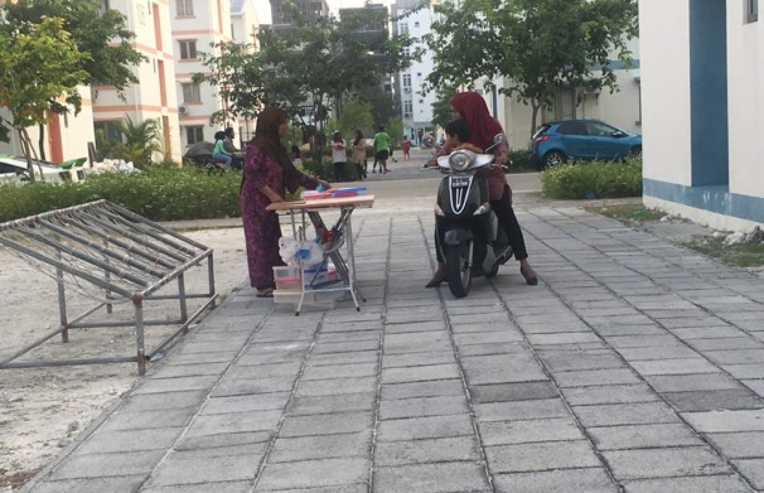 މަގުމަތިން ސައިކަލްގައި ދިޔަ އަންހެނަކު، މޭޒެއް ކައިރިއަށް މަޑުކޮށް، ހެދިކާ ގަންނަނީ.