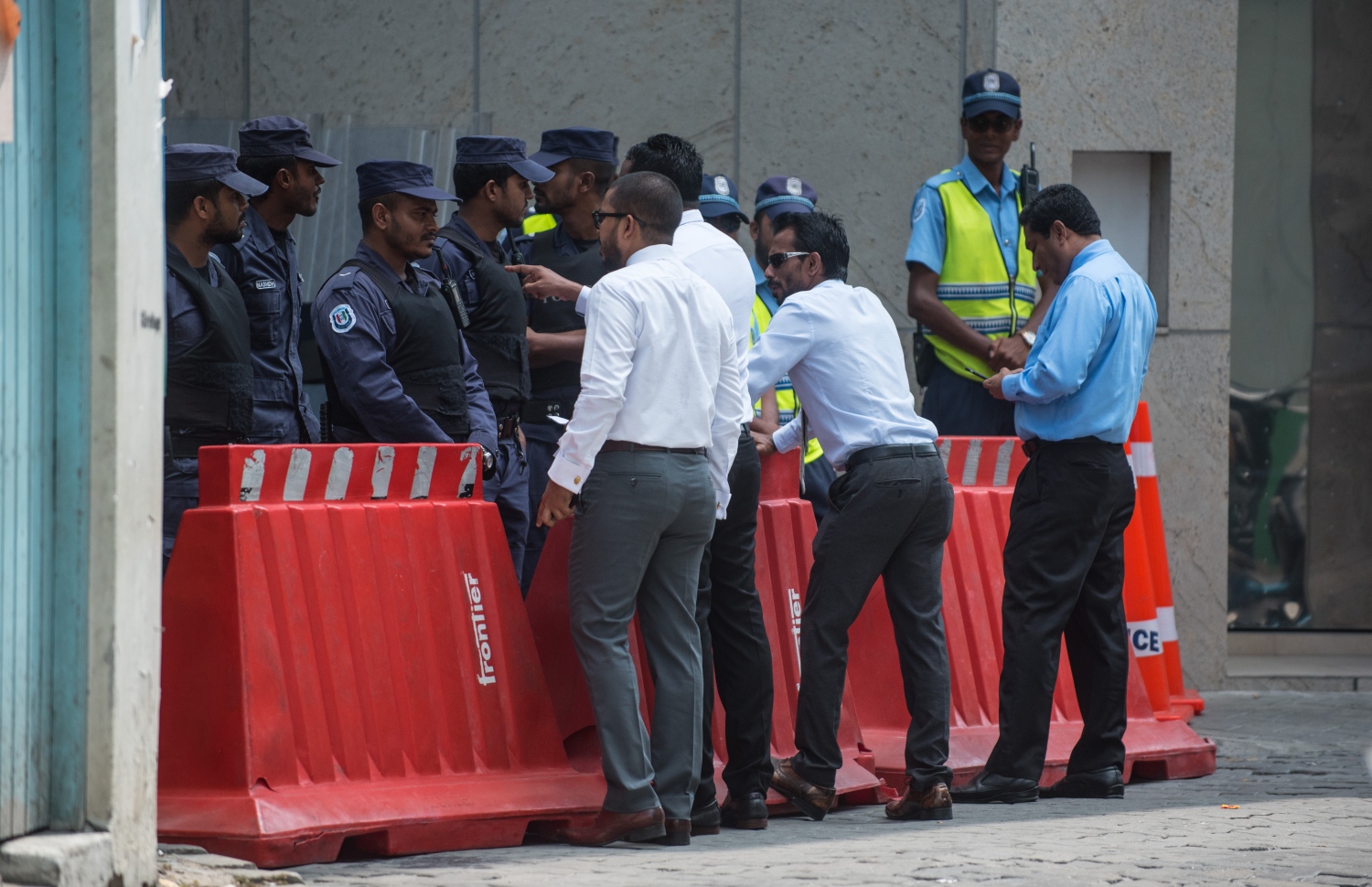 މާލެ: ފެބްރުއަރީ 19، 2018- ކުއްލި ނުރައްކަލުގެ ހާލަތުގެ ގަރާރާ މެދު ރައްޔިތުންގެ މަޖިލީހުން ގޮތެއް ނިންމުމަށް ބާއްވާ ޚާއްސަ ޖަލްސާ އަށް ދައުވަތު ލިބިވަޑައިނުގެންނެވި 12 މެމްބަރުންގެ ތެރެއިން ބައެއް ބޭފުޅުން ބޭރުގައި މަޑުކޮށްލައިގެން ތިއްބެވިއިރު، ފުލުހުން އެ ސަރަހައްދުގެ މަގު ބަންދުކޮށްގެން.---ފޮޓޯ: ހުސެއިން ވަހީދު/މިހާރު