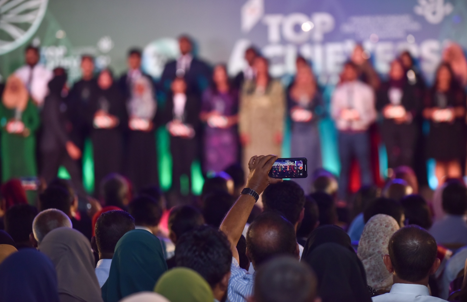 މާލެ: މާޗް 4، 2018- މިދިޔަ އަހަރުގެ އޭ ލެވެލް އިމްތިހާނުގެ ގަދަ 10 ގައި ހިމެނުނު ދަރިވަރުން އިނާމާއެކު ސްޓޭޖުމަތީގައި އެތުރިގެން ތިބިއިރު، މީހަކު އޭނާގެ މޮބައިލް ފޯނުން އެ ދަރިވަރުންގެ ފޮޓޯއެއް ނަގަނީ.---ފޮޓޯ: ހުސައިން ވަހީދު/މިހާރު