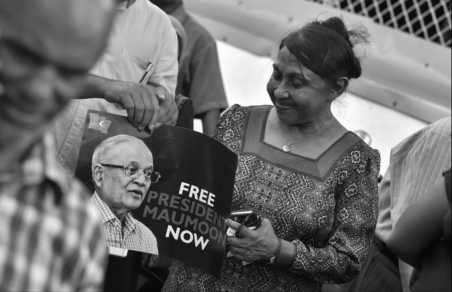 މާލެ: 20 މާޗު 2018: ފިރިކަލުން މައުމޫން ހައްޔަރުކުރުމަށްފަހު ކްރިމިނަލް ކޯޓަށް ހާޒިރުކުރެވުނު އިރު އަނބިކަނބަލުން ނަސްރީނާ އެސަރަހައްދުގައި އެއްވެ ތިބި މީހުންނާއެކު މަގުމައްޗަށް ނިކުންނަވައި، މައުމޫން މިނިވަން ކުރުމަށް ގޮވާލާފައިވާ ޕޯސްޓަރެއް ހިފަހައްޓަވައިގެން.---ފޮޓޯ: ހުސެއިން ވަހީދު/މިހާރު