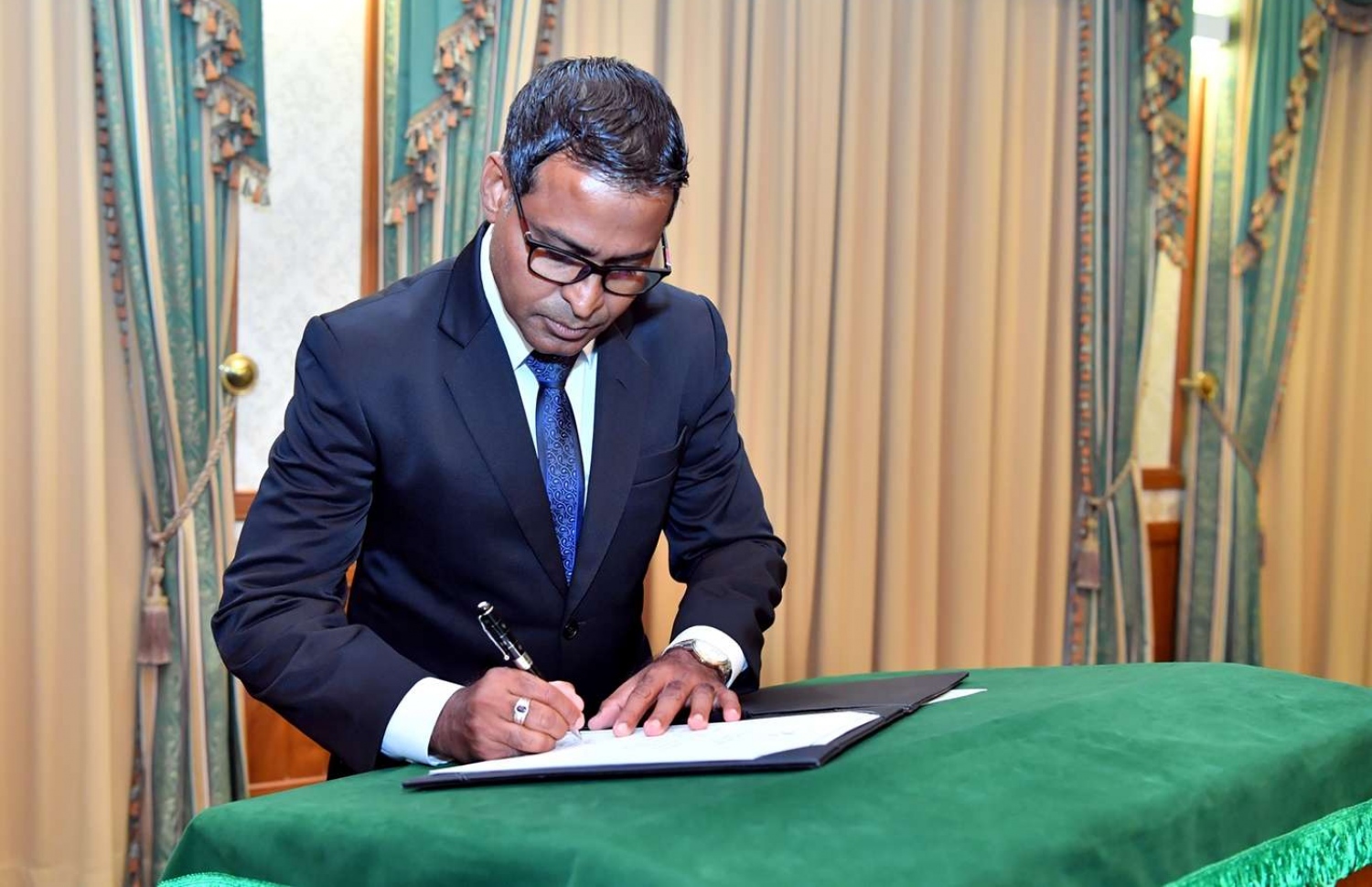 މާލެ: ޖޫން 28، 2018: ސުޕްރީމް ކޯޓުގެ ފަނޑިޔާރު ކަމަށް އައްޔަން ކުރެއްވި ފަނޑިޔާރު އަބްދުލް ޣަނީ މުހައްމަދު މަގާމުގެ ފަތްކޮޅުގައި ސޮއި ކުރައްވަނީ.-- ފޮޓޯ: ރައީސް އޮފީސް