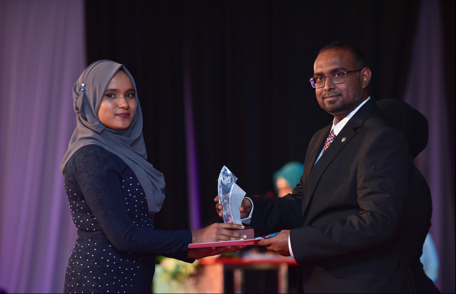 މާލެ: ޖުލައި 9، 2018: މިދިޔަ އަހަރުގެ އޮކްޓޯބަރު/ނޮވެމްބަރުގައި ބޭއްވި އޭ ލެވެލް އިމްތިހާނުން ވަނަތައް ހޯދި ދަރިވަރުންނަށް އެވޯޑު ދިނުމުގެގޮތުން ދަރުބާރުގޭގައި ބޭއްވި ރަސްމިއްޔާތުގައި، ރައީސް އޮފީހުގެ ސްޓޭޓް މިނިސްޓަރު މުޖުތާޒް، ދަރިވަރަކަށް އެވޯޑު ހަވާލުކުރައްވަނީ.--- ފޮޓޯ: ހުސައިން ވަހީދު/މިހާރު