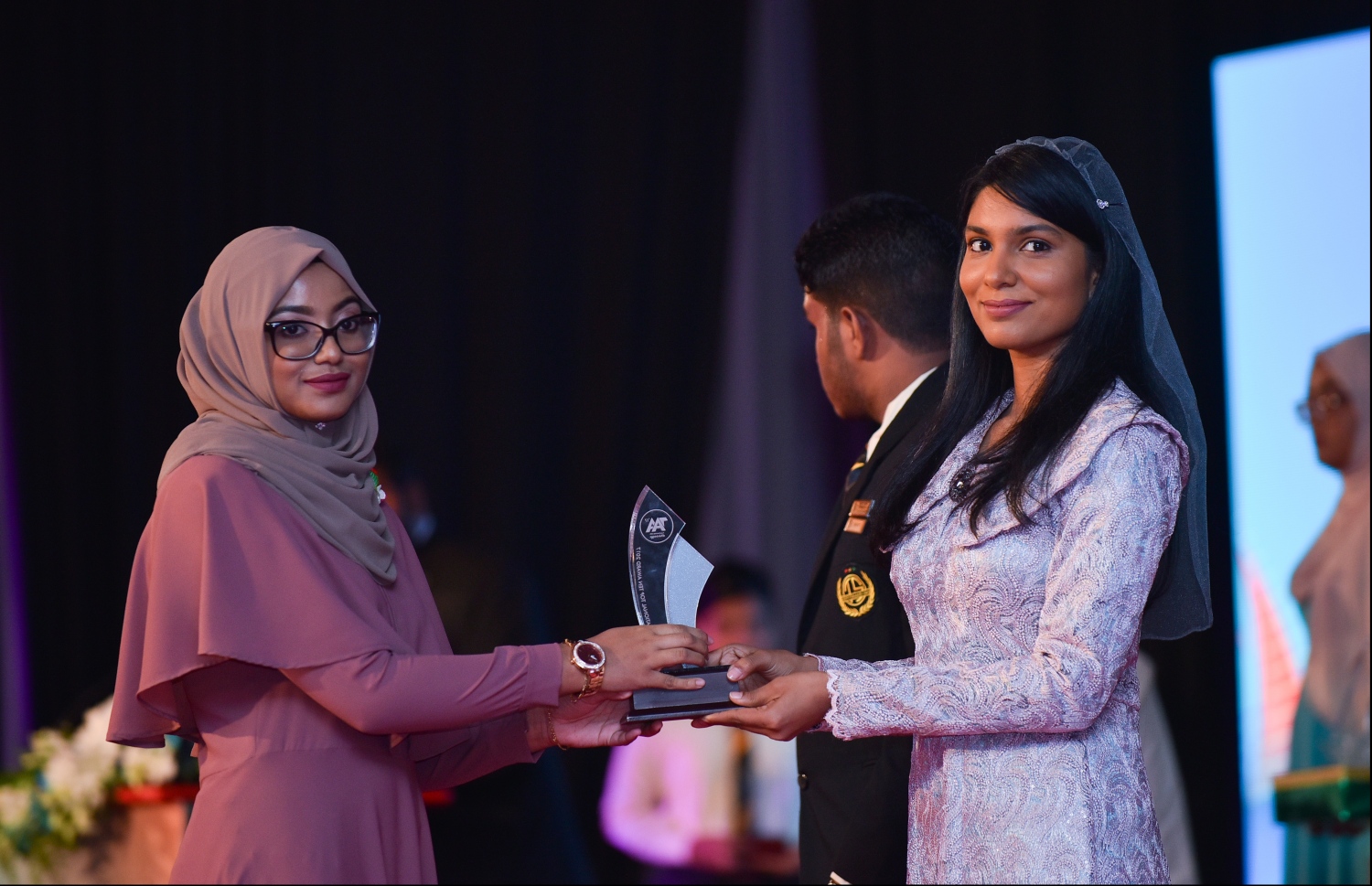 މާލެ: ޖުލައި 9، 2018: މިދިޔަ އަހަރުގެ އޮކްޓޯބަރު/ނޮވެމްބަރުގައި ބޭއްވި އޭ ލެވެލް އިމްތިހާނުން ވަނަތައް ހޯދި ދަރިވަރުންނަށް އެވޯޑު ދިނުމުގެގޮތުން ދަރުބާރުގޭގައި ބޭއްވި ރަސްމިއްޔާތުގައި، ޖެންޑާ މިނިސްޓަރު ޒެނީޝާ ޝަހީދު ޒަކީ، ދަރިވަރަކަށް އެވޯޑު ހަވާލުކުރައްވަނީ.--- ފޮޓޯ: ހުސައިން ވަހީދު/މިހާރު