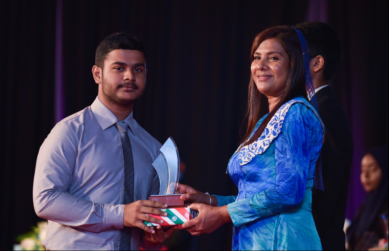 މާލެ: ޖުލައި 9، 2018- މިދިޔަ އަހަރުގެ އޮކްޓޯބަރު/ނޮވެމްބަރުގައި ބޭއްވި އޭ ލެވެލް އިމްތިހާނުގެ ރަންވަނަތައް ހޯދި ދަރިވަރުންނަށް އިނާމު ދިނުމަށް ދަރުބާރުގޭގައި ބޭއްވި ރަސްމިއްޔާތުގައި، އެޑިއުކޭޝަން މިނިސްޓަރު އާއިޝަތު ޝިހާމް، ދަރިވަރަކަށް އެވޯޑާއި އިނާމު ދެއްވަނީ.---ފޮޓޯ: ހުސެއިން ވަހީދު/މިހާރު