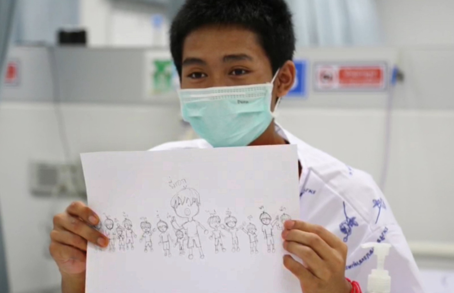 ހޮހަޅައިން ސަލާމަތް ކުރި އަދުލް ސަމޮން، 14، ކުރަހާފައިވާ އެ ކުދިންނާއި ކޯޗުގެ ކާޓޫނެއް ދައްކާލަނީ. --ފޮޓޯ: ތައިލެންޑް ހެލްތު މިނިސްޓްރީ