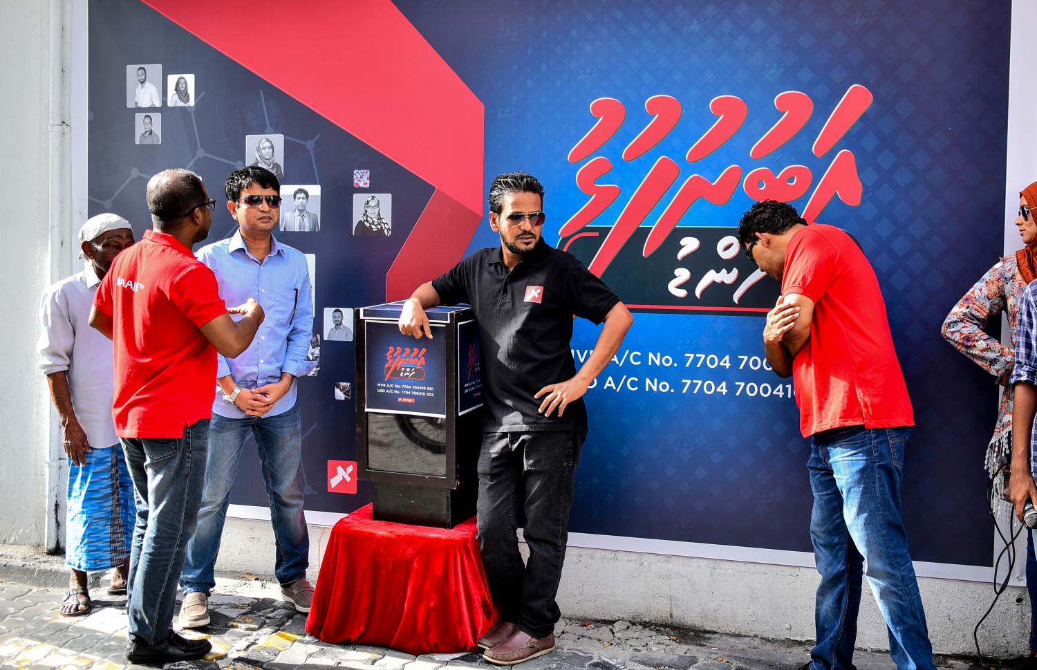 މާލެ: އޮގަސްޓް 10، 2018- އިދިކޮޅު ކޯލިޝަނުން ބޭއްވި މުޒާހަރާއެއްގައި ދެއްކި ވާހަކަތަކެއް ބްރޯޑްކާސްޓް ކުރުމުން ދެ މިލިއަން ރުފިޔާއިން ޖޫރިމަނާ ކޮށްފައިވާ ރާއްޖެ ޓީވީ އަށް އެ ފައިސާ ހޯދައިދޭން "އަބުރުފުޅު ފަންޑު" ގެ ނަމުގައި ފޮއްޓެއް ހުޅުވުމަށް، އެ ސްޓޭޝަން ހިންގާ އިމާރާތުގެ ކުރިމަތީގައި ބޭއްވި ހަފުލާ ފެށުމުގެ ކުރިން، ރާއްޖެ ޓީވީގެ ބައެއް އިސްވެރިން މަޑުކޮށްލައްވައިގެން.---ފޮޓޯ: އަހުމަދު ނިޝާތު/މިހާރު