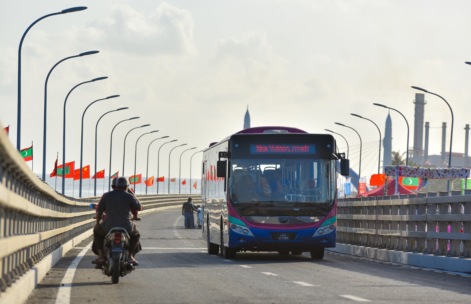 މާލެ އާއި ހުޅުލެއާ ދެމެދު އަޅާފައިވާ ސިނަމާލެ ބްރިޖުގައި ވެހިކަލްތަކަށް ހަދާފައިވާ ހަތަރު ލޭންގެ ތެރެއިން ހުޅުލެ ކޮޅަށް ދުއްވާ ލޭނެއްގައި ބަހެއް ދުއްވާފައި ދާއިރު ބްރިޖުގެ ބައެއް މަސައްކަތްތަކުގައި އުޅޭ ބަޔަކު ބަހުގެ ކައިރިން ސައިކަލެއްގައި ދަނީ. ބްރިޖުގެ ބަސް ދަތުރުތައް ކުރުމަށް ހަމަޖެހިފައިވާ އެމްޕީއެލުން ދަތުރުތަކަށް ޖުމްލަ 22 ބަސް ބޭނުންކުރާ ގޮތަށް ހަމަޖެހިފައިވޭ. އޭގެ ތެރޭގައި 50-70 މީހުންގެ ޖާގައިގެ ބަހާއި 80-100 މީހުންގެ ޖާގައިގެ ދެ ބުރި ބަސްތަކުގެ އިތުރުން 30 މީހުން އުފުލޭ ކުދި ބަސްތަކެއް ވެސް ބޭނުންކުރަން ނިންމާފައިވޭ..---ފޮޓޯ: ހުސައިން ވަހީދު/މިހާރު