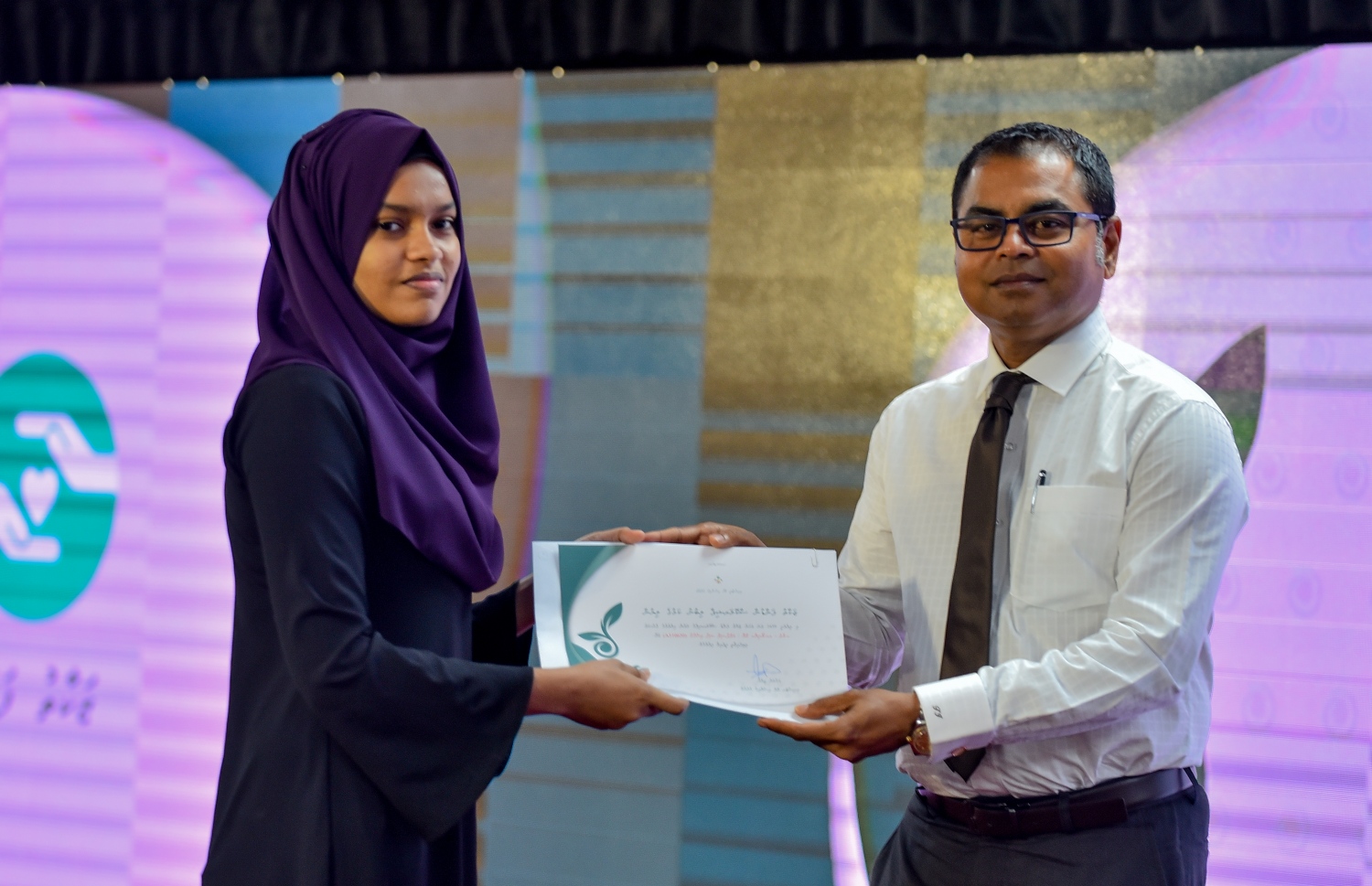 މާލެ: ސެޕްޓެމްބަރު 10، 2018: ޒަކާތު ފަންޑުގެ އެހީގައި ދޭ ސްކޮލަޝިޕްގެ ލިޔުން ހަވާލުކުރުމަށް އިސްލާމީ މަރުކަޒުގައި ބޭއްވި ހާއްސަ ރަސްމިއްޔާތުގައި ސްކޮލަޝިޕް ލިބުނު ދަރިވަރަކަށް، އެންވާރްމަންޓް މިނިސްޓަރު ތޯރިގް(ކ) ލިޔުން ހަވާލުކޮށްދެއްވަނީ.-- ފޮޓޯ: އަހުމަދު ނިޝާތު /މިހާރު