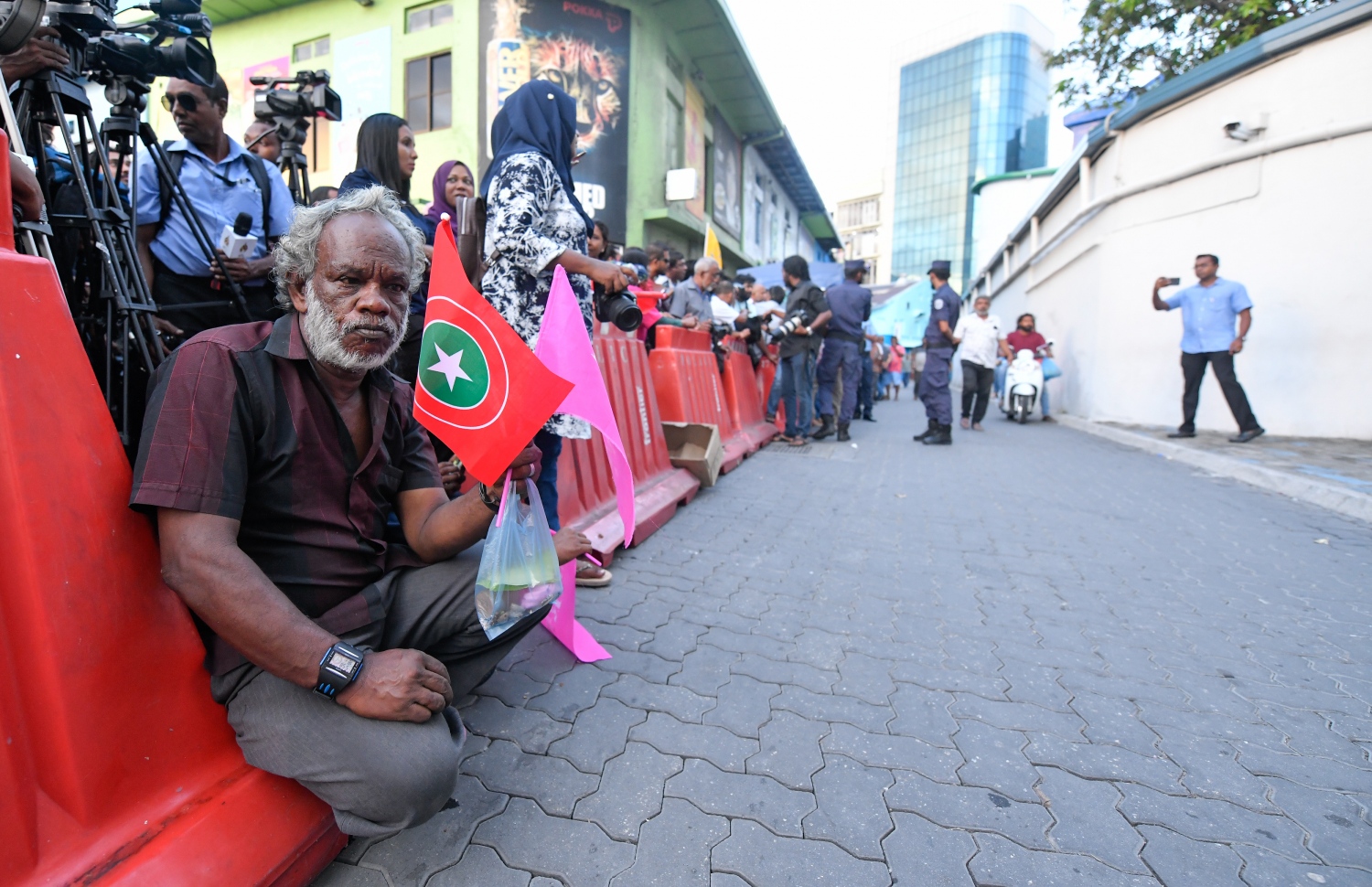 ސެޕްޓެމްބަރު 24، 2018- ކްރިމިނަލް ކޯޓު ސަރަހައްދު: ޝަރީއަތް ނިމެންދެން ބަންދުކޮށްފައި ތިބި ސިޔާސީ ބައެއް ބޭފުޅުން މިނިވަންކުރުމާ ގުޅިގެން ކްރިމިނަލް ކޯޓު ސަރަހައްދައް އެއްވެފައިތިބި މީހުންގެ ތެރެއިން މީހަކު ބެރިކޭޑެއްގެ ކައިރި އިށީނދެލައިގެން.---ފޮޓޯ: ހުސައިން ވަހީދު/މިހާރު