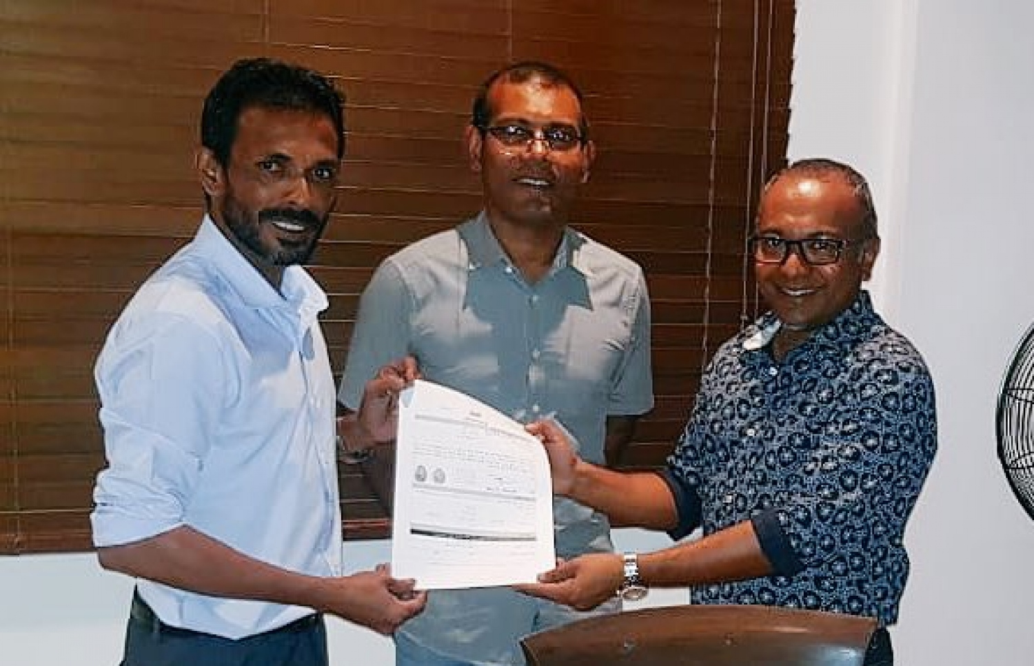 އިހަވަންދޫ ދާއިރާގެ މެމްބަރު މުހައްމަދު އަބްދުﷲ އެމްޑީޕީއަށް ރޭ ސޮއިކުރެއްވުމަށް ފަހު އޭނާގެ ފޯމު އެ ޕާޓީގެ ޗެއާޕާސަން ހަސަންއާ ހަވާލުކުރައްވާއިރު، ފަހަތުގައި ނަޝީދު ހުއްޓިވޑައިގެން.---ފޮޓޯ: އެމްޑީޕީ