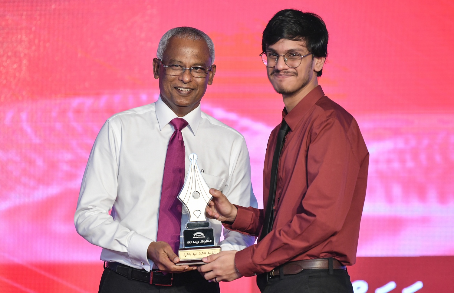 މާލެ: ޑިސެމްބަރު 11، 2018: ރާއްޖޭގެ ނޫސްވެރިކަމަށް 75 އަހަރު ފުރުމުގެ އަލިމަސްޔޫބީލް ފާހަގަ ކުރުމަށާއި ނޫސްވެރިކަމުގެ މިދިޔަ އަހަރުގެ އިނާމުތައް ދިނުމަށް މޯލްޑިވްސް މީޑިއާ ކައުންސިލާއި ހޯމް މިނިސްޓްރީ ގުޅިގެން ބޭއްވި ޖަލްސާގައި ނޫސްވެރިކަމުގެ ރަން ގަލަން ހާސިލްކުރެއްވި "އާފަތިސް" ނޫހުގެ އެޑިޓަރު އަބްދުﷲ ނައީމް އިބްރާހީމްގެ އެވޯޑު އޭނާގެ ދަރިފުޅަށް ރައީސް އިބްރާޙިމް މުހައްމަދު ސޯލިހް ހަވާޅުކުރައްވަނީ.---ފޮޓޯ: އަހުމަދު ނިޝާތު/މިހާރު