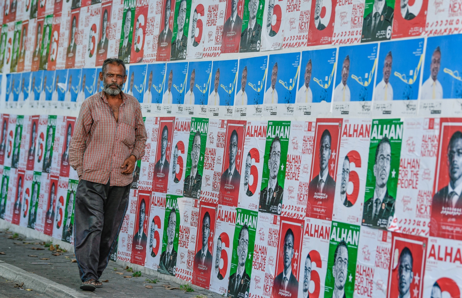 ގިނައަދަދަކަށް ޕޯސްޓަރު ހަރުކޮށްފައިހުރި ފާރެއްގެ ކައިރިން މީހަކު ހިނގާފައި އަންނަނީ.---ފޮޓޯ: ނިޝާން އަލީ/މިހާރު