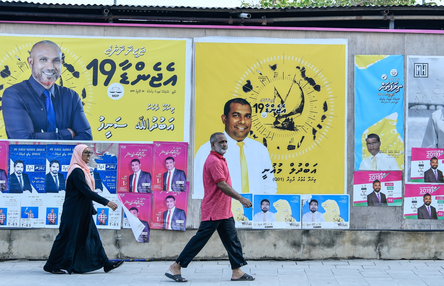 ގިނަ އަދަދެއްގެ ކެމްޕޭން ޕޯސްޓަރާއި ބިލްބޯޑު ހަރުކޮށްފައި ހުރި ގެއެއްގެ ކައިރި މަގުމަތީގައި މީހުން ހަރަކާތްތެރިވަނީ.---ފޮޓޯ: ނިޝާން އަލީ/މިހާރު