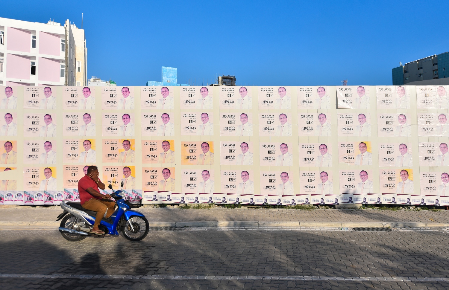 ގިނަ އަދަދެއްގެ ކެމްޕޭން ޕޯސްޓަރު ހަރުކޮށްފައިހުރި ފާރެއްގެ ކައިރިން މީހަކު ސައިކަލެއްގައި ދަނީ.---ފޮޓޯ: ހުސައިން ވަހީދު/މިހާރު