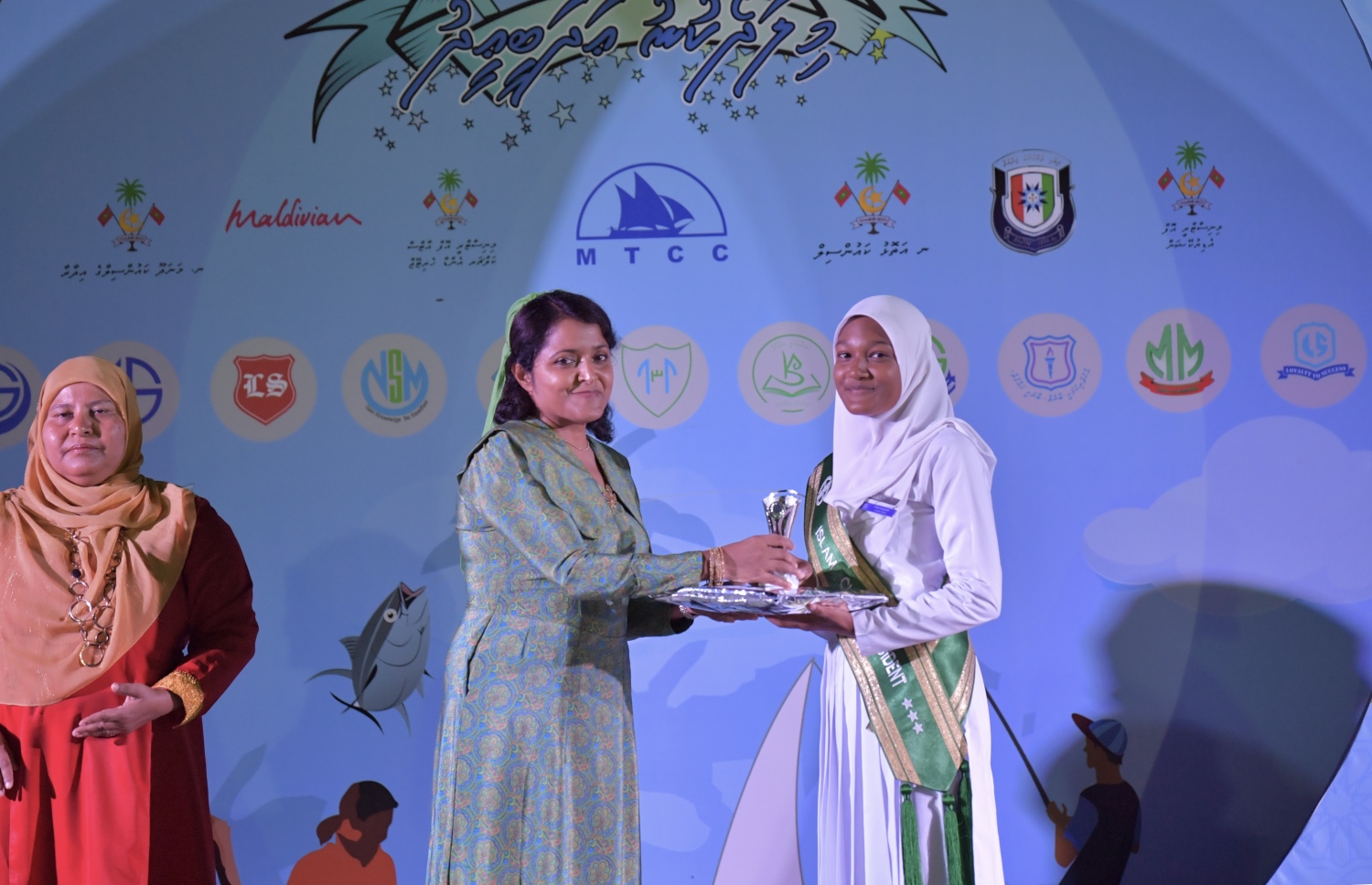 ނ. މަނަދޫ: ސެޕްޓެމްބަރު 14، 2019: މަނަދޫ ބަނދަރު ސަރަޙައްދުގައި ބޭއްވި 'މިލަދެކުނު އަދަބީ އީދު 2019'  ނިންމުމުގެ ޖަލްސާގައި އެ ސްކޫލުގެ ދަރިވަރަކަށް ހެރިޓޭޖް އެންޑް އާޓްސް މިނިސްޓަރު ޔުމްނާ މައުމޫން އިނާމު ހަވާލުކޮށްދެއްވަނީ.-- ފޮޓޯ: ރައީސް އޮފީސް