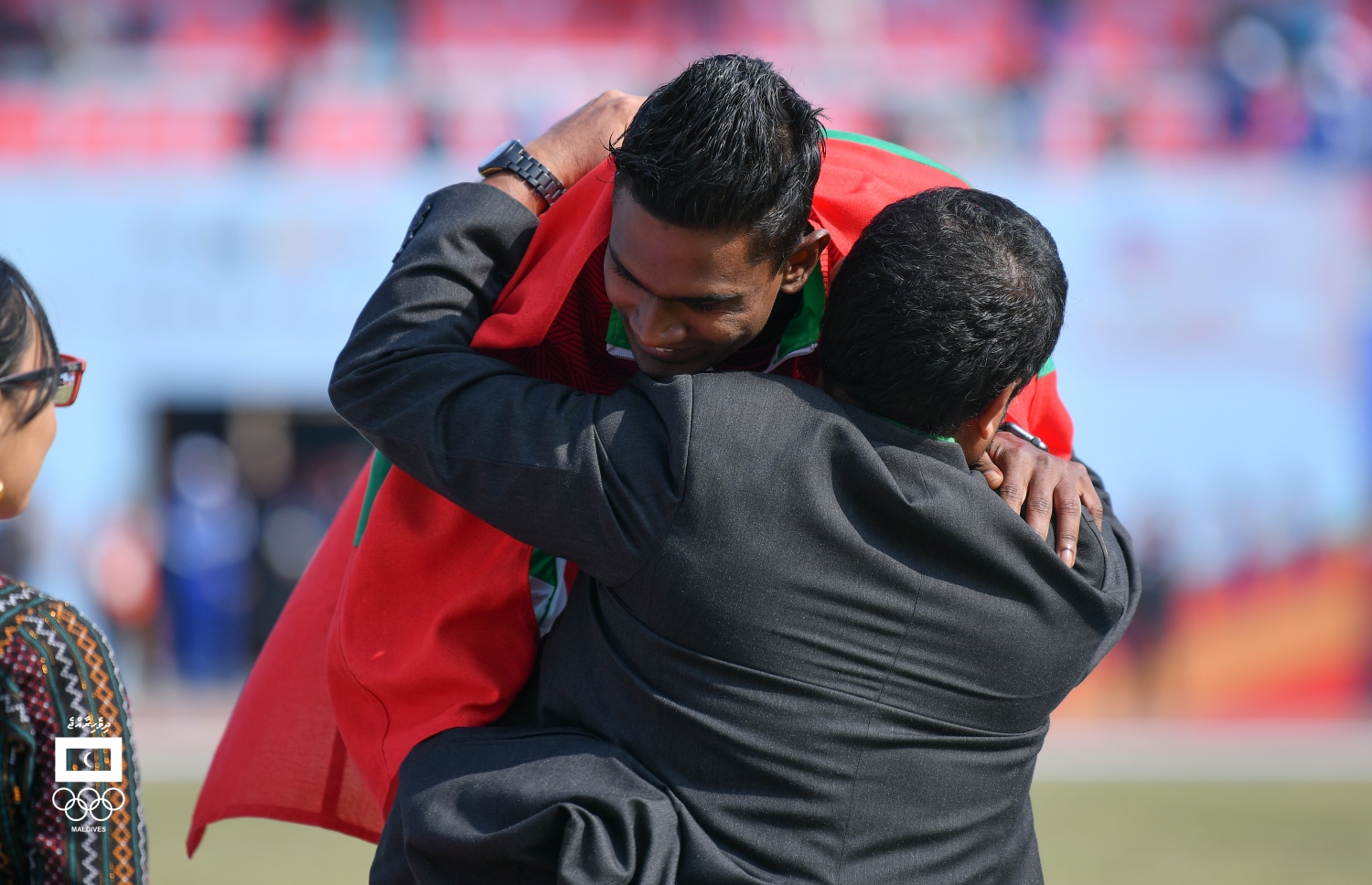 ހަސަން ސާއިދުގެ ކަރުގައި ރަން މެޑަލް އެޅުވުމަށް ފަހު ޝަރަފްވެރި މެހެމާން ރާއްޖޭގެ އެތުލެޓިކްސް އެސޯސިއޭޝަނުގެ ރައީސް ތޮލާލް އޭނާގެ ގައިގައި ބައްދާލަނީ. --އެމްއޯސީ ފޮޓޯ: ހުސެއިން ވަހީދު