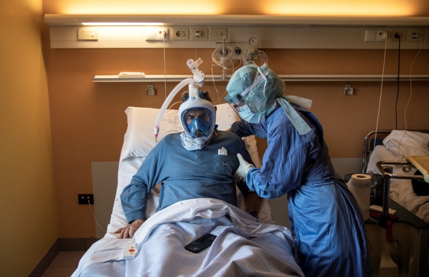 އިޓަލީ: އޭޕްރިލް 7، 2020: އިޓަލީގައި ކޮވިޑް-19 ބަލީގައި ފަރުވާދެމުންދާ ބަލިމީހެއްގެ ގައިގައި ނަރުހަކު  މާސްކު އަޅައިދިނުމަށް އެހީތެރިވަމުންދާއިރު، ރައްކާތެރިވުމުގެ ގޮތުން ނަރުސް، މާސްކާއި އަންގިއާއެކު މުޅިގައި އެއްކޮށް ކަވަރުކޮށްފައި.-- ފޮޓޯ: އޭއެފްޕީ