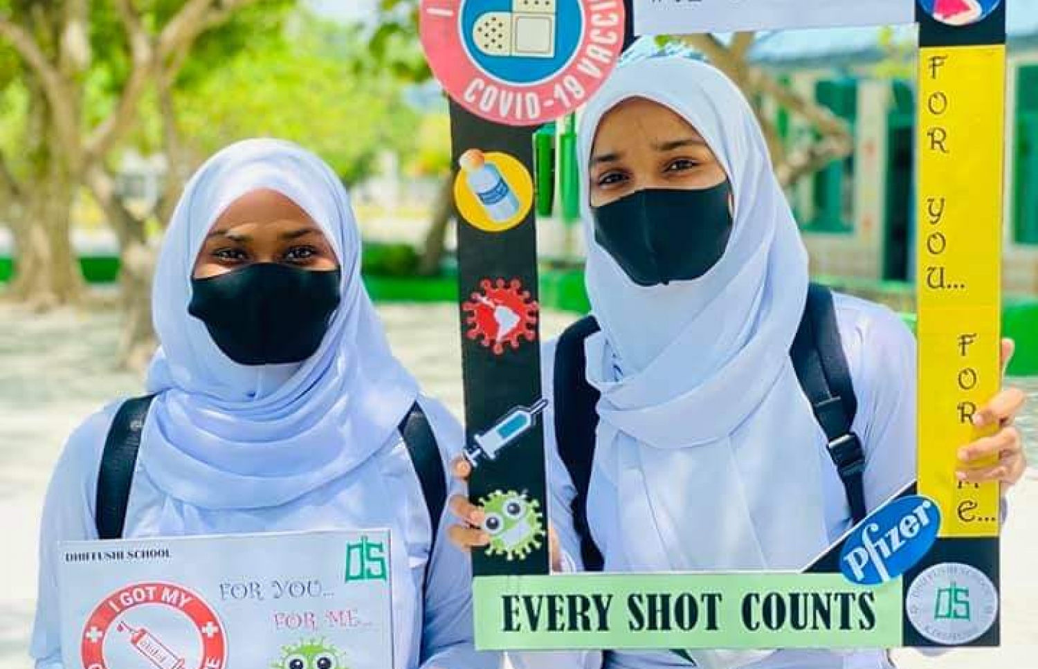 ސްކޫލެއްގެ ދެ ދަރިވަރަކު، ވެކްސިން ޖެހުމަށް ހިތްވަރުދީ ބޯޑެއް ހިފަހައްޓައިގެން.- ފޮޓޯ: އެޑިއުކޭޝަން މިނިސްޓްރީ