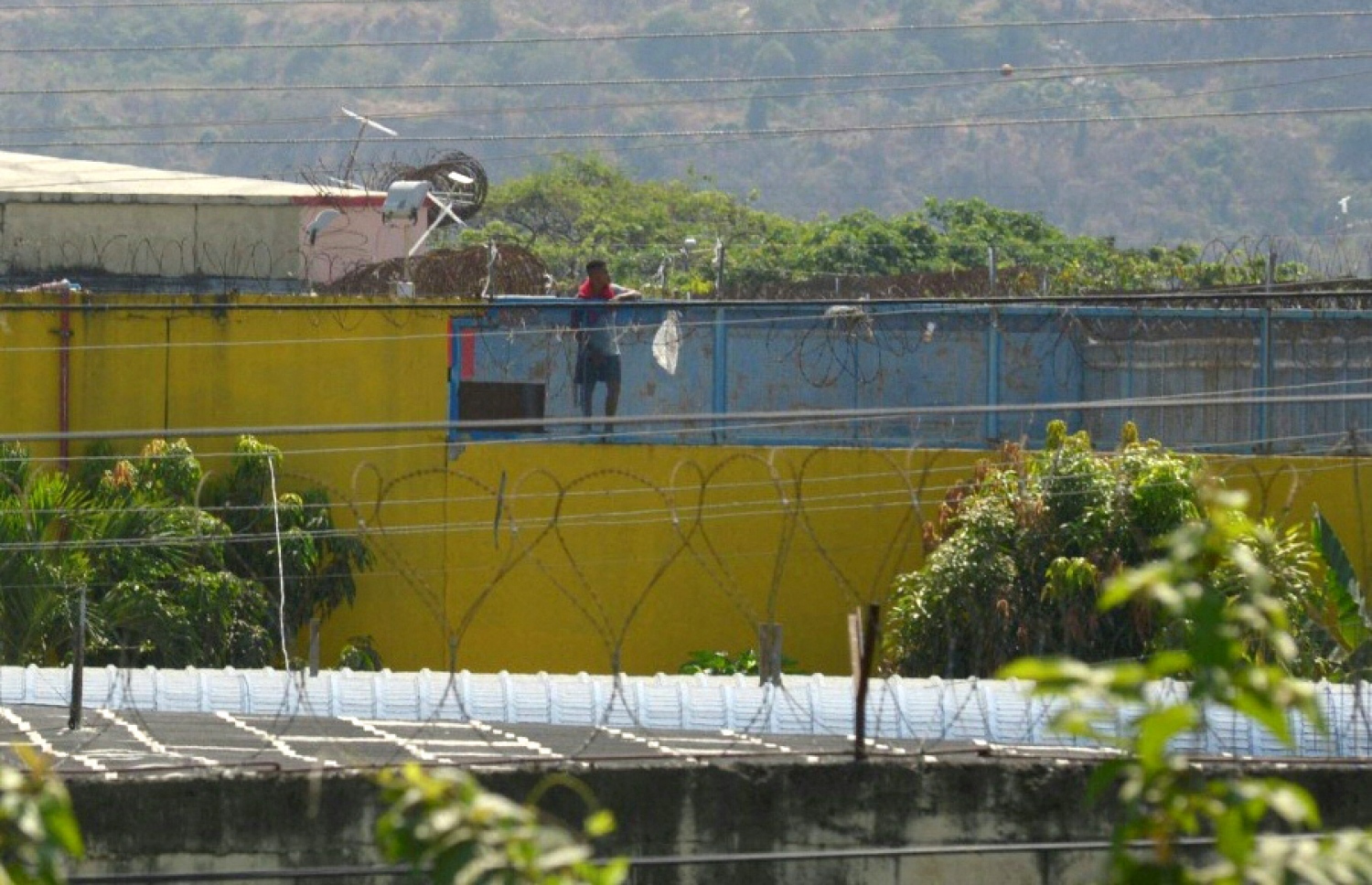 ހަމަނުޖެހުން ހިންގި ޖަލުގެ ފުރާޅުމަތީގައި ޖަލުގެ ގައިދީއަކު، ޖަލުގެ ބޭރުގައި ސިފައިންނާއި ފުލުހުންގެ ހަރަކާތްތައް ހުރި ގޮތް ބަލަނީ. --އޭއެފްޕީ