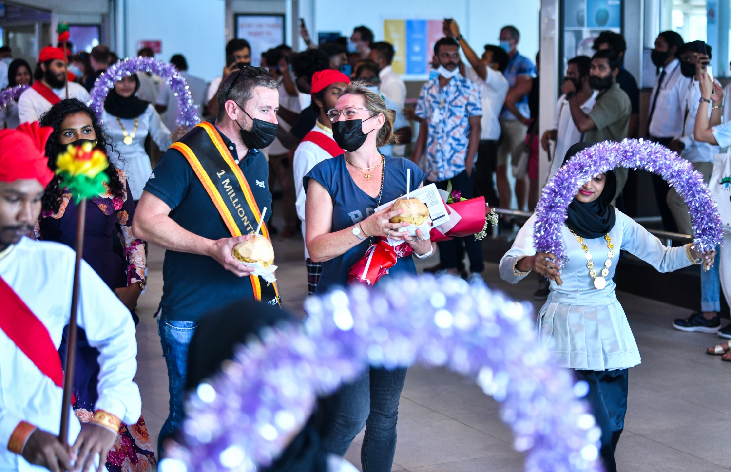 ވެލާނާ އެއާޕޯޓް: އޮކްޓޫބަރު 29، 2021- މި އަހަރު ރާއްޖެ އައި އެއް މިލިއަން ވަނަ ޓޫރިސްޓް ފްރާންސްގެ ވިންސެންޓް ވިކްޓާ ކޮރެން ޕިޓާއޫ އާއި އޭނާގެ އަންހެނުން އެއާޕޯޓުގެ އެރައިވަލް ޓާމިނަލުން ނުކުމެގެންދާއިރު ދިވެހި ސަގާފީ އައިޓަމަކުން މަރުހަބާ ކިޔަނީ--- ފޮޓޯ: ފަޔާޒު މޫސާ / މިހާރު