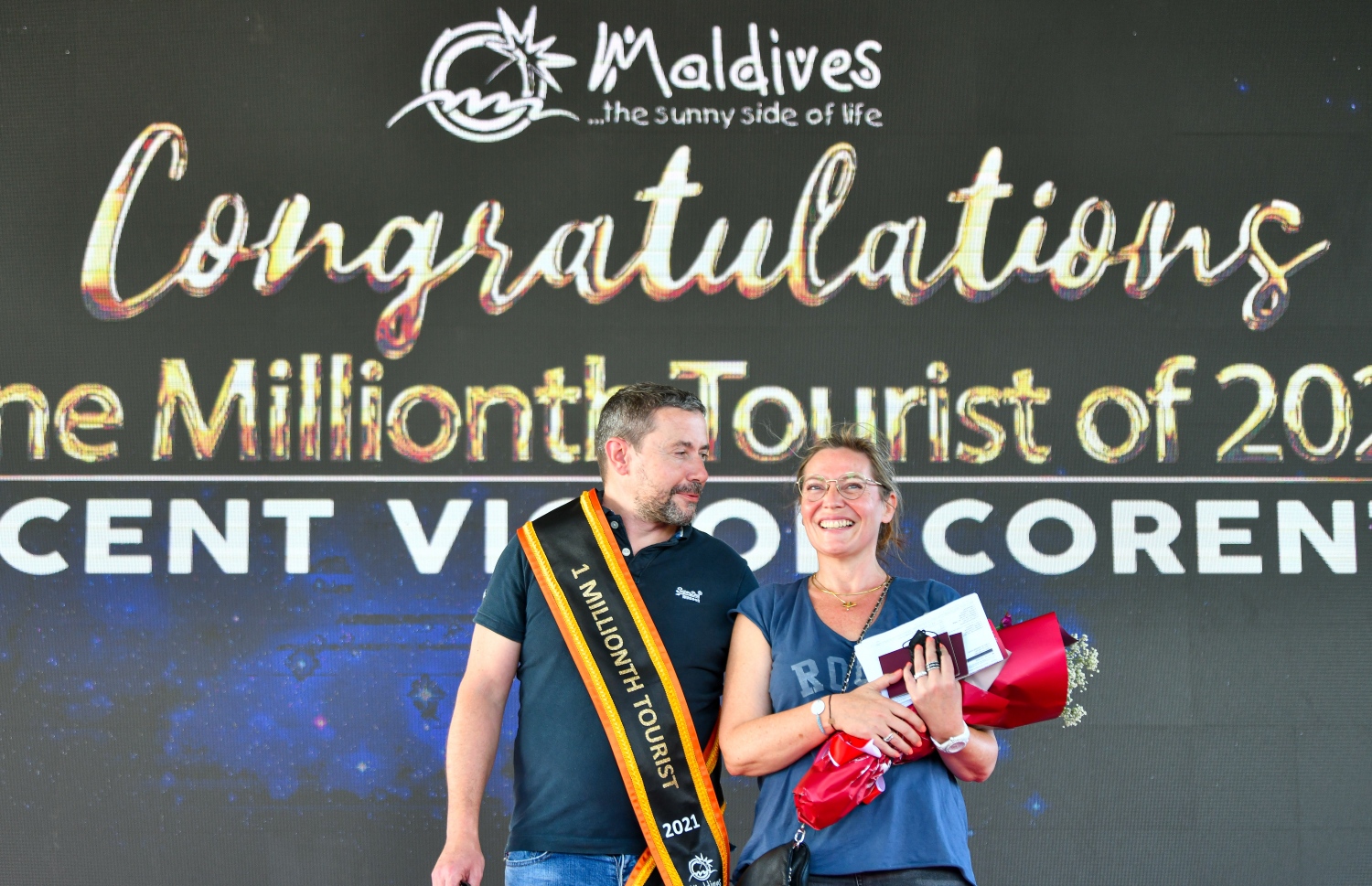 ވެލާނާ އެއާޕޯޓް: އޮކްޓޫބަރު 29، 2021- މި އަހަރު ރާއްޖެ އައި އެއް މިލިއަން ވަނަ ޓޫރިސްޓް ފްރާންސްގެ ވިންސެންޓް ވިކްޓާ ކޮރެން ޕިޓާއޫ އާއި އޭނާގެ އަންހެނުންގެ ޝަރަފުގައި ދިވެހި ސަގާފީ ހަރަކާތެއް ހުށަހަޅާއިރު، އެކަމާ އުފާކޮށް ދެ މީހުން ވާހަކަ ދައްކަނީ.--- ފޮޓޯ: ފަޔާޒު މޫސާ / މިހާރު