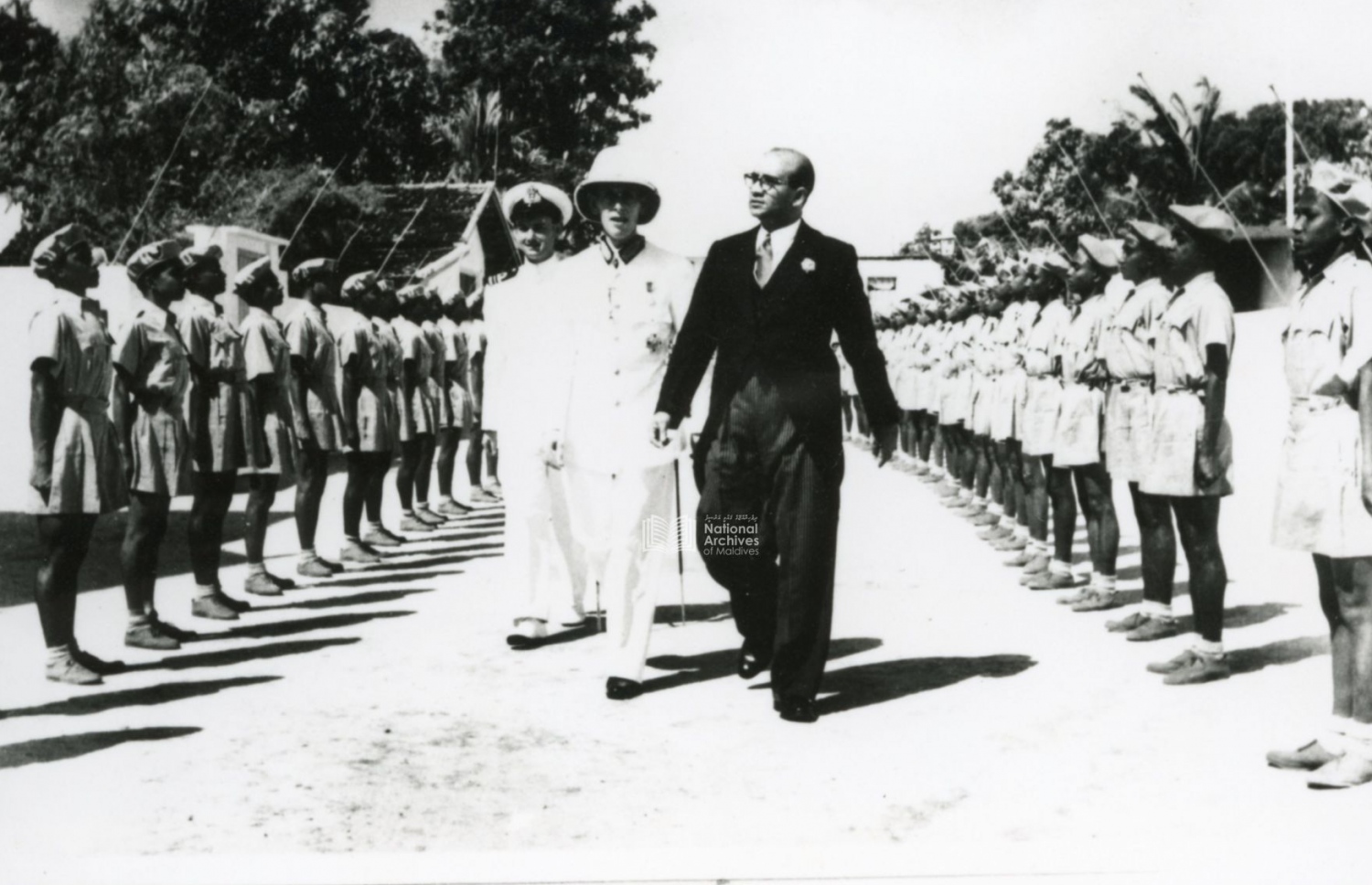 ޖުމްހޫރީ ދުވަހު ރައީސް މުހައްމަދު އަމީން މުލީއާގެއަށް ވަޑައިގަންނަވަނީ. އަމީންގެ ފަހަތްޕުޅުގައި އެ ހުންނެވީ އިނގިރޭސި ހައި ކޮމިޝަނަރު ހެނކިންސަން. -- ފޮޓޯ: ނެޝަނަލް އާކައިވް