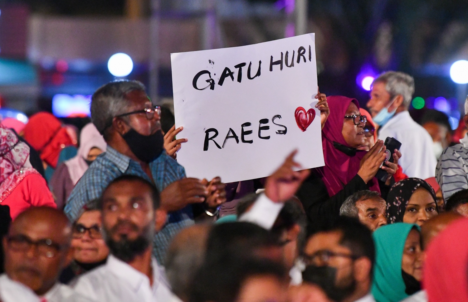 ޑިސެމްބަރު 3، 2021- ކުރީގެ ރައީސް އަދި އިދިކޮޅު ލީޑަރު އަބްދުﷲ ޔާމީންގެ މައްޗަށް މަނީލޯންޑަރުންގެ ކުށް ސާބިތުވެ، ފަސް އަހަރަށް ޖަލަށް ލާން ނޮވެމްބަރު 28، 2019 ގައި ކުރި ހުކުމުން ސަލާމަތްވުމާ ގުޅިގެން، އެ މަނިކުފާނަށް މަރުހަބާ ކިޔަން ބޭއްވި ބިޔަ ޖަލްސާ އަށް ދިޔަ މީހަކު، އެ މަނިކުފާނުގެ ކެރުމާއި ހިތްވަރަށްޓަކައި "ގަޓު ހުރި ރައީސް" ޖަހާފައިވާ ޕޯސްޓަރެއް ދައްކައިލަނީ: ޔާމީނާއެކު ދެ އަހަރު ފަހުން، މާލޭގެ ކާނިވާ ސަރަހައްދުގައި ބޭއްވި މި ޖަލްސާ އަށް ވަރަށް ގިނަ ބަޔަކު ދިޔަ.---ފޮޓޯ: ފަޔާޒު މޫސާ/ މިހާރު