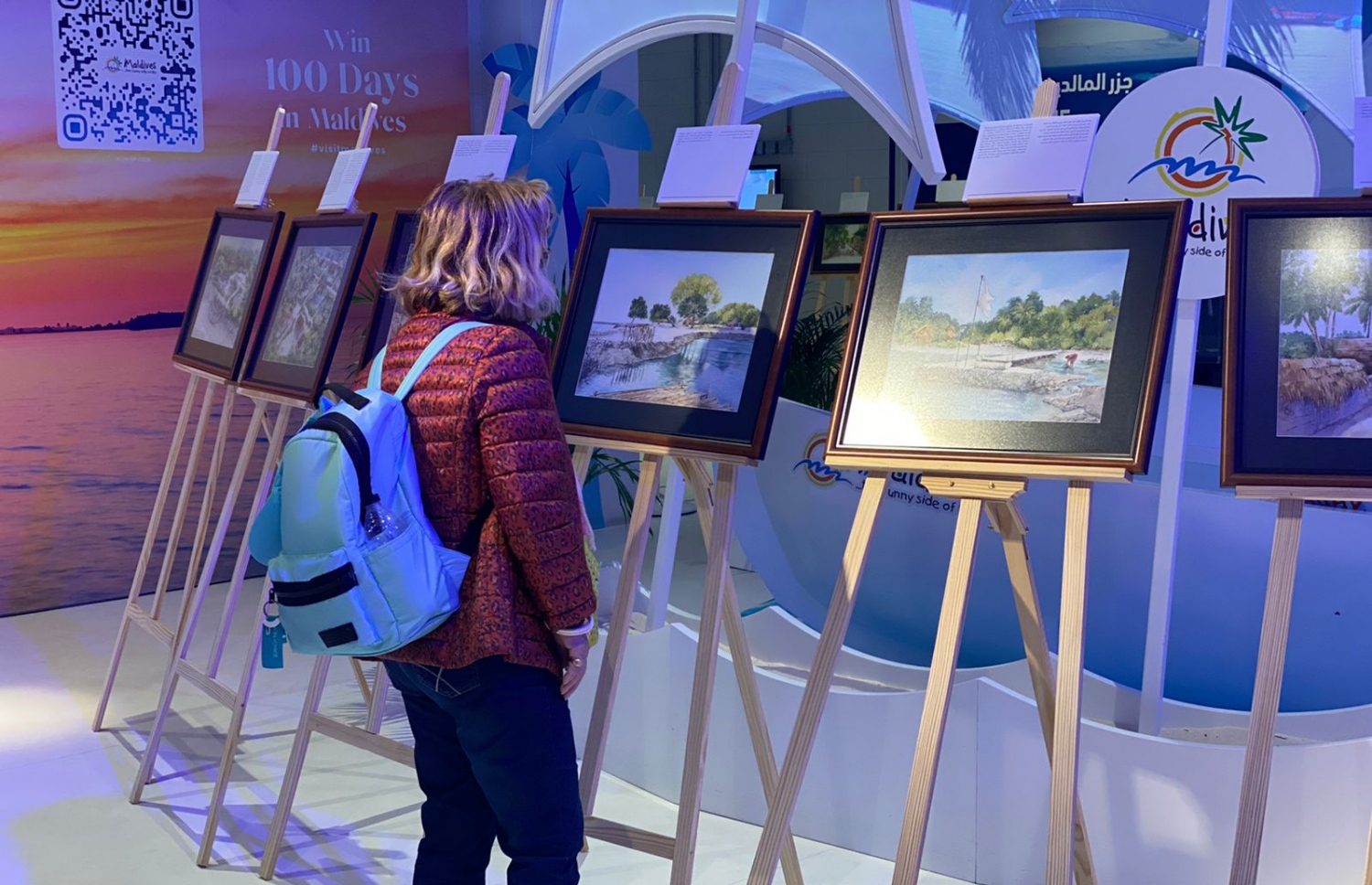 ދުބާއީ އެކްސްޕޯ 2020 ގައި ބޭއްވި އައިމިނަތު ޝިމްހާ ޝަކީބްގެ "މާލޭގެ ކިއްލާ" އާޓް އެގްޒިބިޝަން ބަލާލަން ދިޔަ މީހަކު އާޓްވޯކްތައް ކައިރީގައި ހުއްޓިލައިގެން.-- ފޮޓޯ: ޝިމްހާ