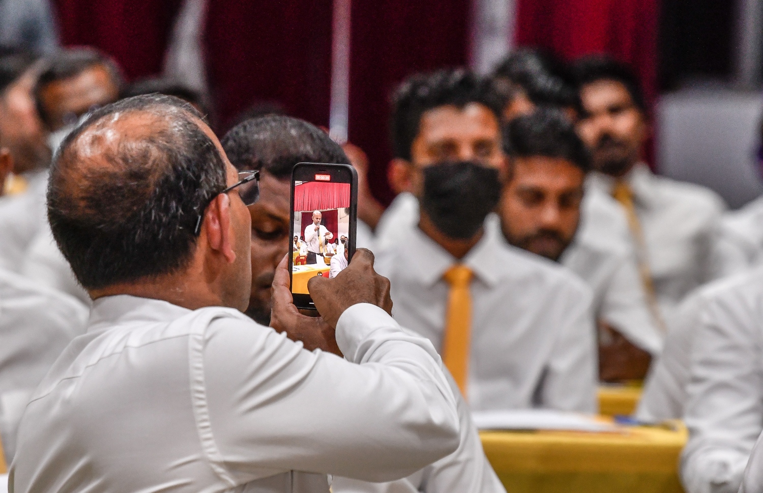 އެމްޑީޕީގެ ގައުމީ މަޖިލީހުގެ ޖަލްސާގައި އެ ޕާޓީގެ ކައުންސިލްގެ މެމްބަރަކު ވާހަކަ ދައްކަވާއިރު އޭނާގެ ފޮޓޯއެއް، އެ ޕާޓީގެ ރައީސް މުހައްމަދު ނަޝީދު ފޯނުން ނަންގަވަނީ.---ފޮޓޯ: ފަޔާޒު މޫސާ / މިހާރު