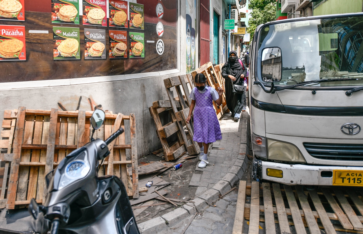 ޕޭވްމަންޓްމަތީގައި ބަހައްޓާފައި ހުރި ޕެލެޓްތަކެއް ކައިރިން ކުޑަކުއްޖަކު ހިނގާފައި އަންނަނީ: މި ޕެލެޓްތަކަކީ، އޭގެ ކުޑައިރުކޮޅެއް ކުރިން މަގުމަތީގައި ޖާގަ ކަށަވަރު ކުރަން ދުރާލައި ބާއްވާފައި ހުރި ޕެލެޓްތަކެއް: އުޅަނދު ޕާކު ކުރުމާ އެކު އެ ޕެލެޓްތައް އެ ހުންނަނީ ދުވާރުމަތީގައި ބަހައްޓާފައި. އާންމުންނަށް ކިތަންމެ ބޮޑު ތަކުލީފެއް މި ޕެލެޓްތަކާ ގުޅިގެން އުފުލަން ޖެހުނަސް ފެންނަނީ ސަރުކާރުގެ ކަމާ ގުޅޭ އިދާރާތަކުގެ ނުކުޅެދުންތެރިކަން.