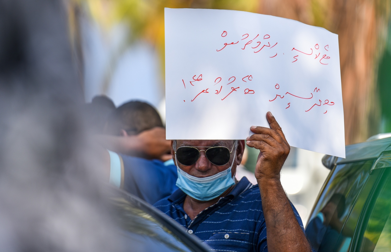 ޓެކްސީ ކުރުމުގައި ބިދޭސީން އުޅޭ ކަމަށް ބުނެ އެ މީހުން އެ ދާއިރާ އިން ބޭރުކުރަން ގޮވާލާ ޕޯސްޓަރެއް ހިފައިގެން ޑްރައިވަރަކު އަޑުއުފުލަނީ: ބިދޭސީން ރާއްޖޭގައި ޓެކްސީގެ ހިދުމަތް ދިނުން މަނާ.---ފޮޓޯ: ފަޔާޒު މޫސާ/މިހާރު