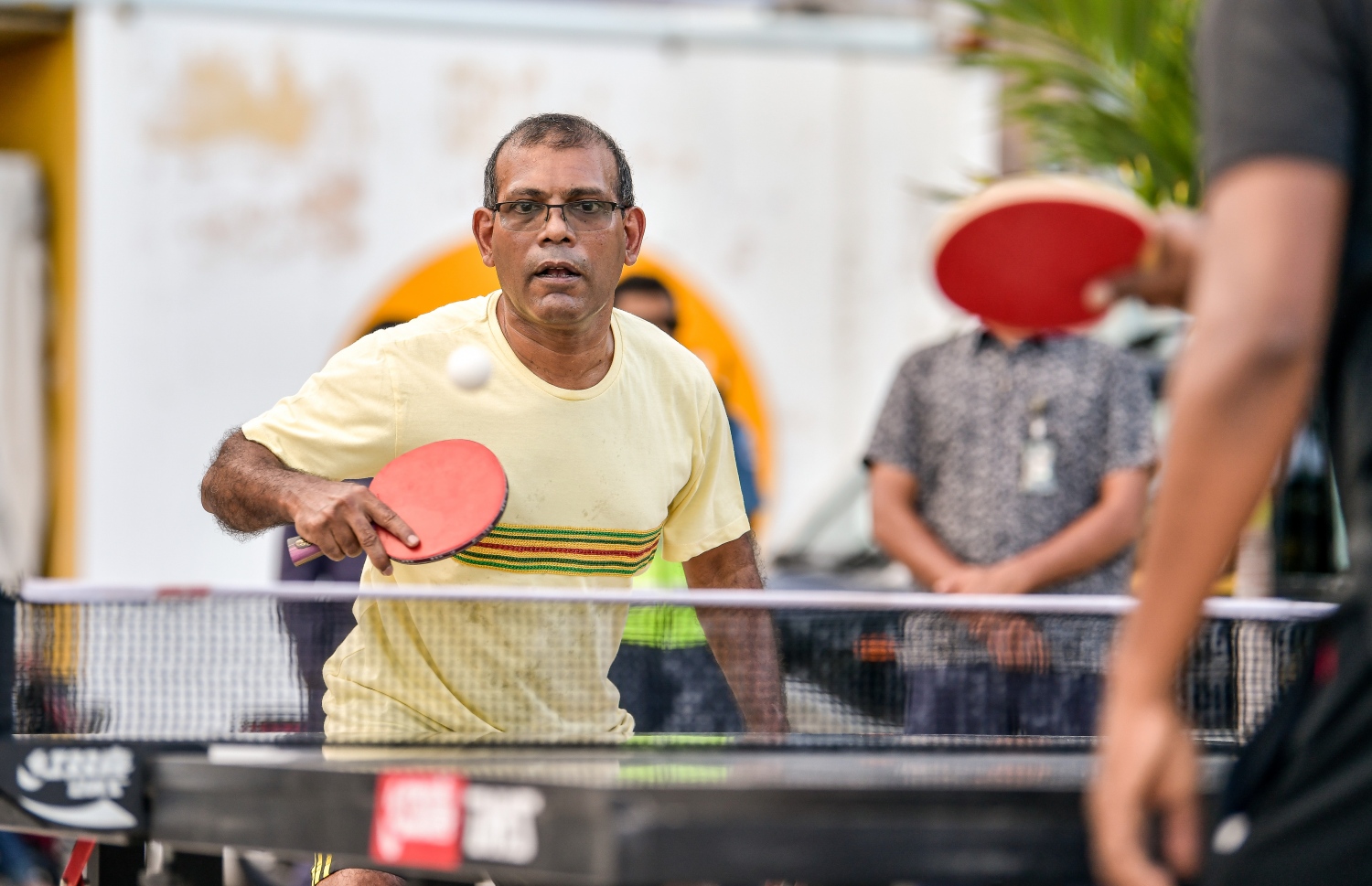 މިދިޔަ ރޯދަ މަހުގެ ތެރޭގައި ނަގާފައިވާ މި ފޮޓޯގައި އެ ފެންނަނީ، ނަޝީދު ޓޭބަލް ޓެނިސް ކުޅުއްވާ މަންޒަރު. އެ މަނިކުފާނުގެ ފުރާނަ ދުއްވާލުމަށް ދިން ހަމަލާ އަށް އަހަރެއް މިއަދު ވާއިރު، މިހާރު އުޅުއްވަނީ ކުރިއެކޭ އެއްގޮތަށް ބިޒީ ޝެޑިއުލެއްގައި. އެކަމަކު، އެ މަނިކުފާނުގެ ފުރާނަ އަށް އޮތް ނުރައްކާ އަދިވެސް ކުޑަ ނޫން ކަމަށް އާއިލާ އިން ބުނޭ. އަދި އާއިލާ އިން ވެސް، އަދި ނަޝީދު ވެސް ގޮވާލައްވަނީ ނުރައްކާތެރި އެ ހަމަލާ އަށް ފަންޑު ކުރި މީހުން ހޯދައިދިނުމަށް. -- ފޮޓޯ: ނިޝާން އަލީ/ މިހާރު