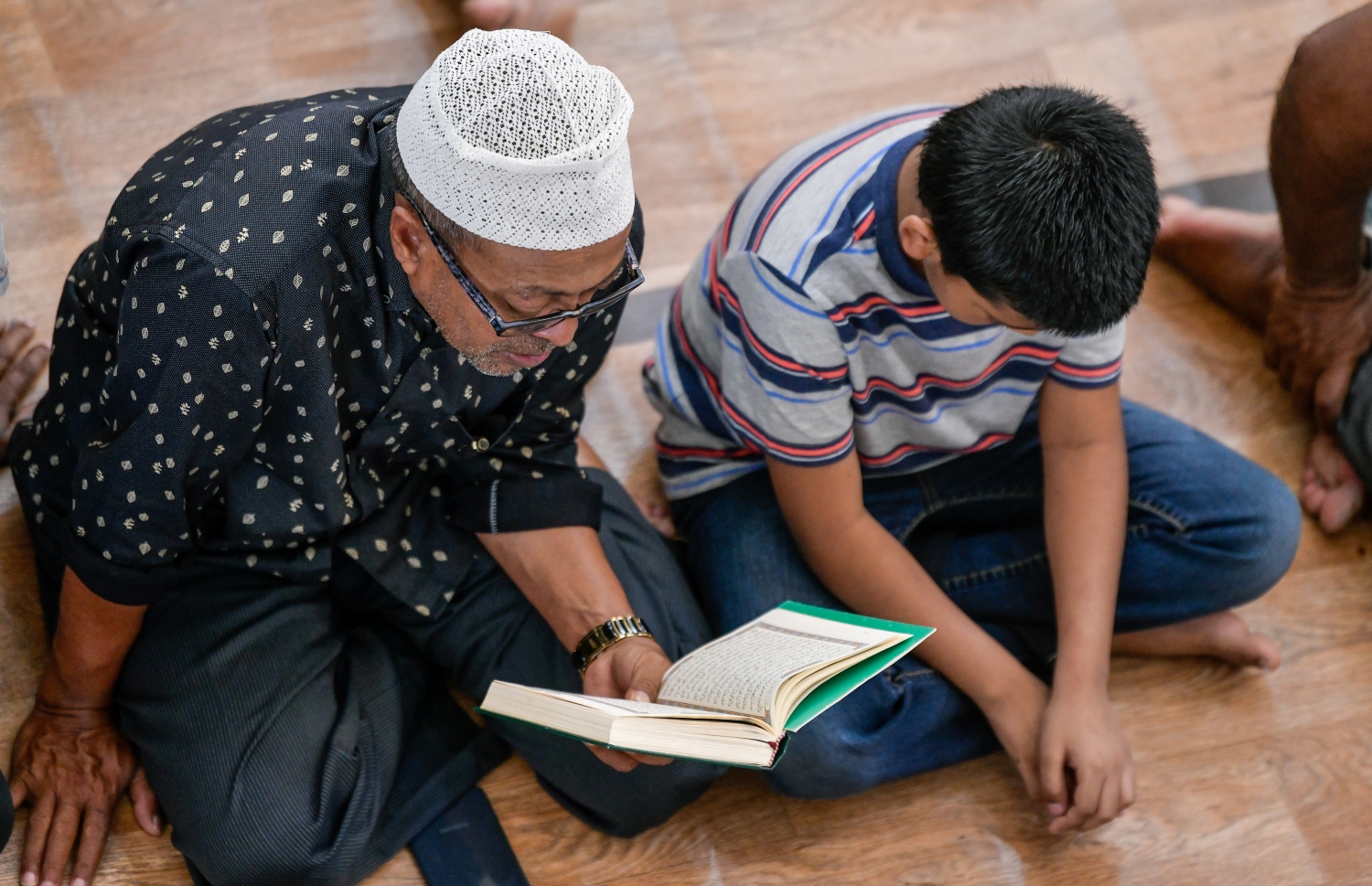 އިސްލާމީ މަރުކަޒުގައި މިއަދު ކުރި ހުކުރު ނަމާދަށް ދިޔަ މީހަކު ގުރުއާން ކިޔަވާއިރު، އޭނާގެ ކައިރީގައި ކުޑަކުއްޖަކު މަޑުކޮށްލައިގެން ގުރުއާން އަޑުއަހަނީ.--- ފޮޓޯ: ފަޔާޒު މޫސާ | މިހާރު