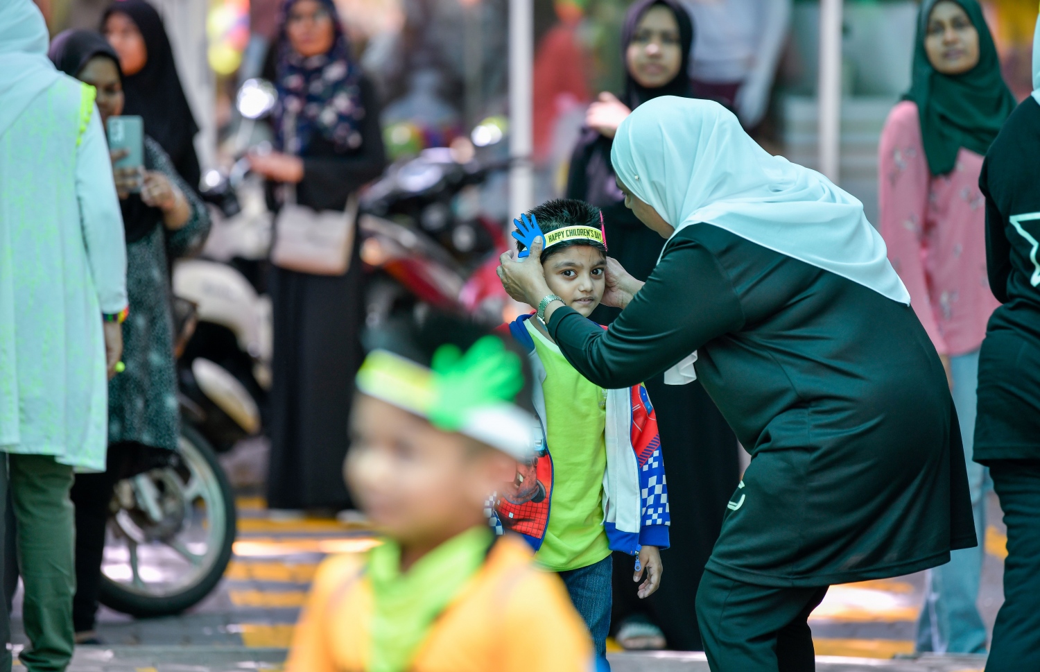 ގަލޮޅު ސްކޫލުގެ އަހަރީ ދުވަހާއި ކުޑަކުދިންގެ ދުވަހާ ގުޅުވައިގެން ގަލޮޅު ސްކޫލުގައި ހާއްސަ ހަރަކާތްތަކެއް ބާއްވާފައިވާއިރު، އެ ދުވަހު ސްކޫލަށް ދިޔަ ކުއްޖެއްގެ ބޮލުގައި ޕްރިންސިޕަލް ސުރައްޔާ ތޮއްޕެއް އަޅުވައިދެނީ: ޕްރިންސިޕަލާއި ޓީޗަރުންގެ ފަރާތުން ކުދިންނަށް ހާއްސަ މަރުހަބާއެއް ކިޔާފައިވޭ.---ފޮޓޯ: ފަޔާޒު މޫސާ| މިހާރު