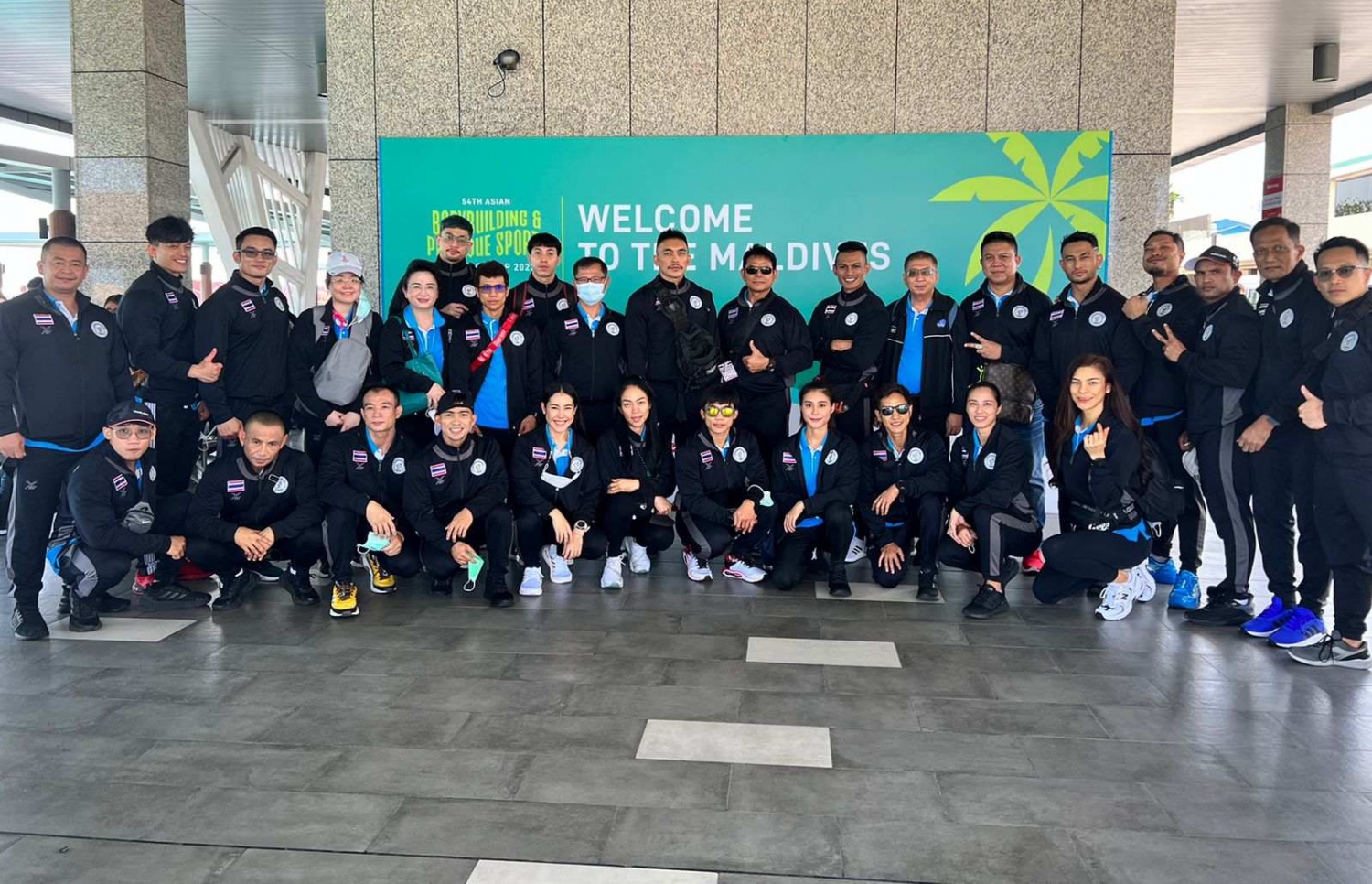 ރާއްޖޭގައި ބާއްވާ 54 ވަނަ އޭޝިއަން ބޮޑީބިލްޑިންގް ޗެމްޕިއަންޝިޕްގައި ވާދަކުރަން އައި ތައިލެންޑްގެ ޓީމު، މުބާރާތް ޕްރޮމޯޓް ކުރަން ވެލާނާ އިންޓަނޭޝަނަލް އެއާޕޯޓުގައި ހަރުކޮށްފައިވާ ބިލްބޯޑް ކައިރީ ފޮޓޯއަކަށް ހުއްޓިގެން: އަންނަ ބުރާސްފަތި ދުވަހުގެ ނިޔަލަށް ކ. މާފުށްޓާއި ކްރޮސް ރޯޑްސް މޯލްޑިވްސްގައި ބާއްވާ މި މުބާރާތަކީ މިހާތަނަށް ރާއްޖޭގައި ބާއްވާ ބައިނަލްއަގްވާމީ އެންމެ ބޮޑު ކުޅިވަރު ހަރަކާތް.--- ފޮޓޯ: ބީބީއޭއެމް