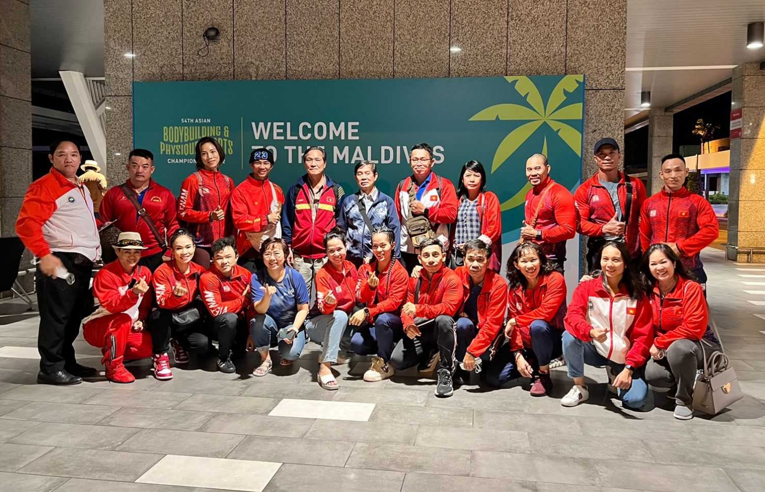 ރާއްޖޭގައި ބާއްވާ 54 ވަނަ އޭޝިއަން ބޮޑީބިލްޑިންގް ޗެމްޕިއަންޝިޕްގައި ވާދަކުރަން އައި ވިއެޓްނާމްގެ ޓީމު، މުބާރާތް ޕްރަމޯޓް ކުރަން ވެލާނާ އިންޓަނޭޝަނަލް އެއާޕޯޓުގައި ހަރުކޮށްފައިވާ ބިލްބޯޑް ކައިރީގައި ފޮޓޯއަކަށް ހުއްޓިގެން: މި މުބާރާތް އޮންނާނީ ކ. މާފުށްޓާއި ކްރޮސް ރޯޑްސް މޯލްޑިވްސްގައި ޖުލައި 15-21 އަށް.--- ފޮޓޯ: ބީބީއޭއެމް