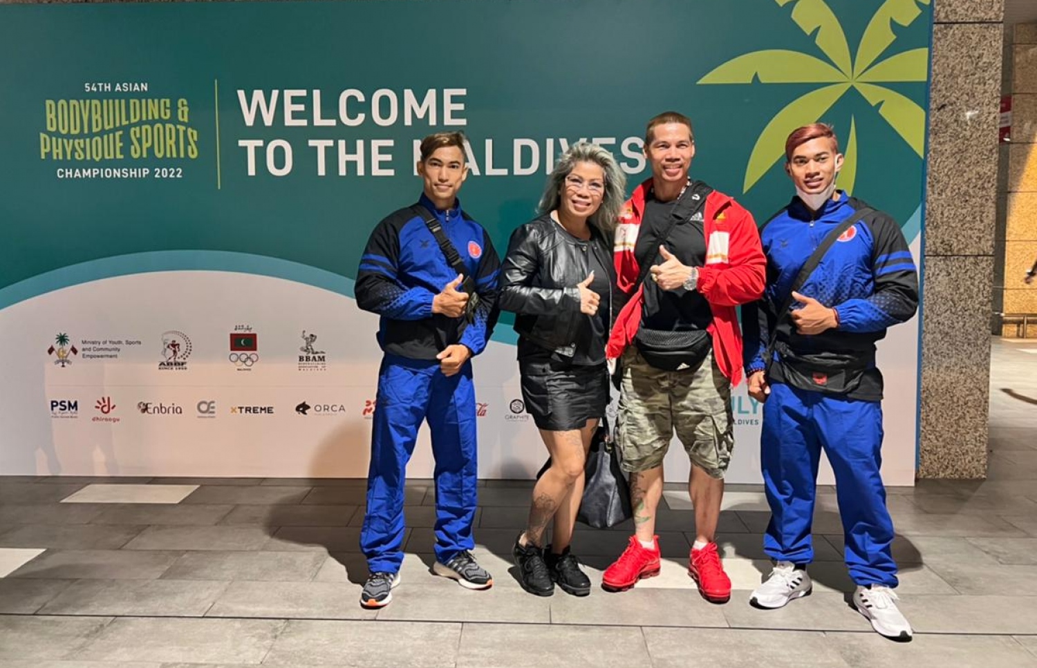 ރާއްޖޭގައި ބާއްވާ 54 ވަނަ އޭޝިއަން ބޮޑީބިލްޑިންގް ޗެމްޕިއަންޝިޕްގައި ވާދަކުރަން އައި ކެމްބޯޑިއާގެ ޓީމުގެ ބައެއް އެތުލީޓުން، މުބާރާތް ޕްރޮމޯޓް ކުރަން ވެލާނާ އިންޓަނޭޝަނަލް އެއާޕޯޓުގައި ހަރުކޮށްފައިވާ ބިލް ބޯޑް ކައިރީގައި ފޮޓޯއަކަށް ހުއްޓިގެން: މި މުބާރާތް އޮންނާނީ ކ. މާފުށްޓާއި ކްރޮސް ރޯޑްސް މޯލްޑިވްސްގައި ޖުލައި 15-21 އަށް.--- ފޮޓޯ: ބީބީއޭއެމް