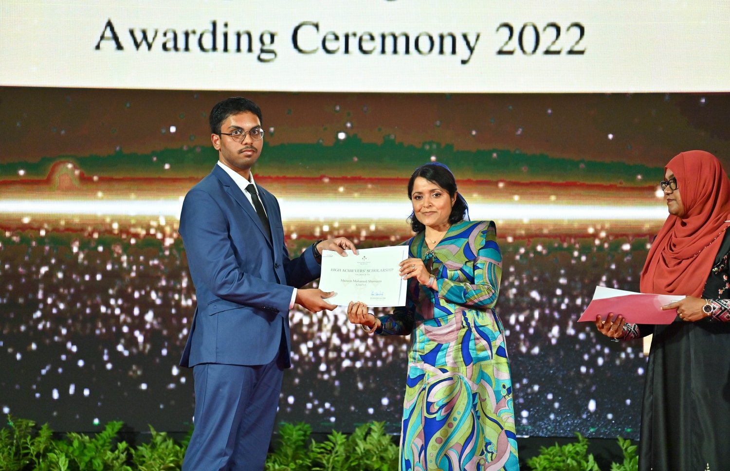 ރައީސް ދެއްވާ ހާއްސަ ސްކޮލަޝިޕާއި ހައި އެޗީވާސް ސްކޮލަޝިޕްގެ ލިޔުން ހަވާލު ކުރުމަށް ގިޔާސުއްދީން ސްކޫލުގައި ބޭއްވި ހަފުލާގައި އާޓްސް އެންޑް ހެރިޓޭޖް މިނިސްޓަރު ދުންޔާ މައުމޫން، ހައި އެޗީވާސް ސްކޮލަޝިޕް ލިބުނު ދަރިވަރަކަށް ލިޔުން ހަވާލު ކުރައްވަނީ.-- ފޮޓޯ: ރައީސް އޮފީސް