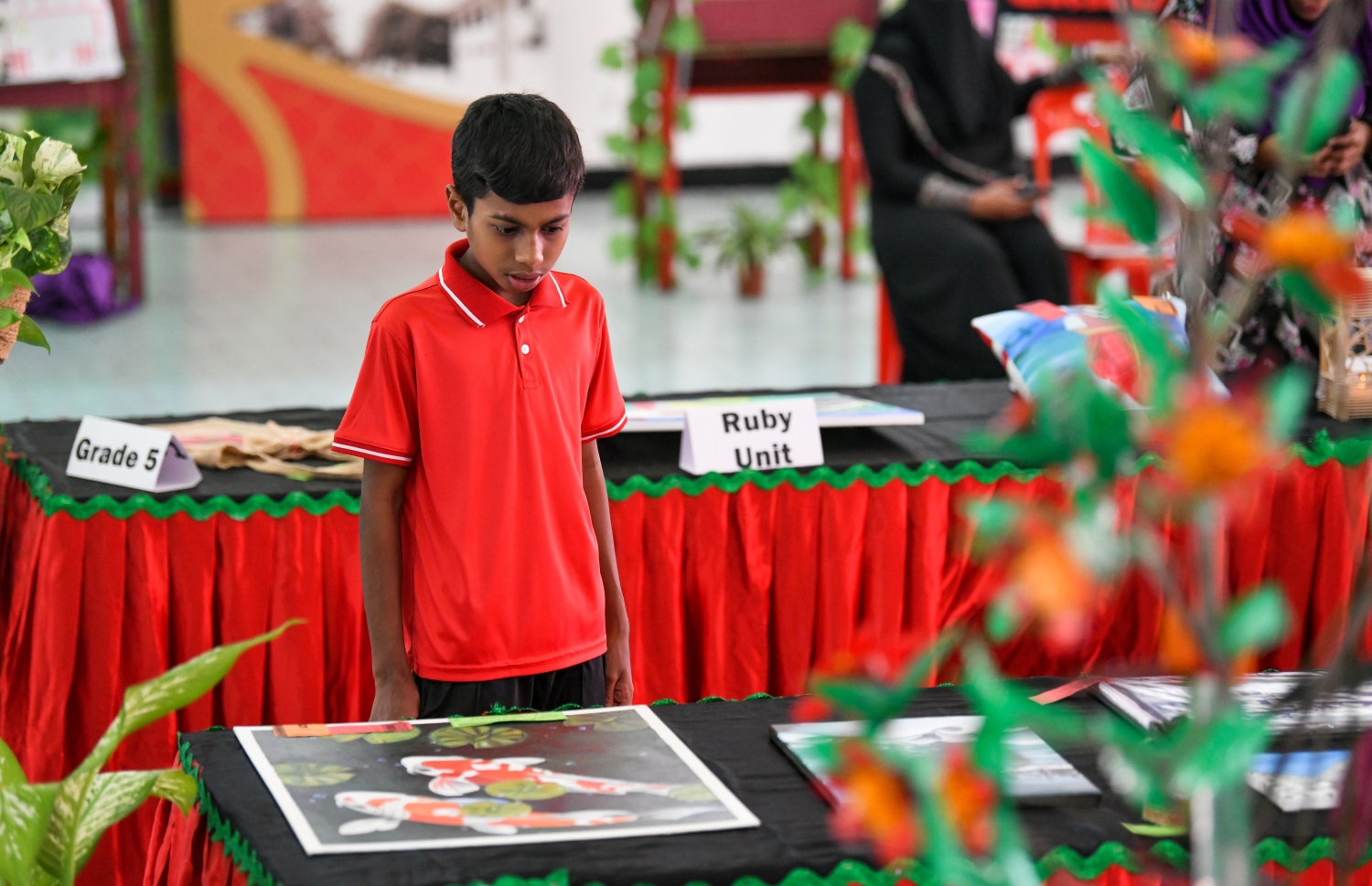 މަޖީދިއްޔާ ސްކޫލްގެ ކުއްޖަކު، އެ ސްކޫލް ހޯލުގައި ކުރިއަށް ގެންދިޔަ މައުރަޒުގައި ހުރި ބައެއް ތަކެތި ބަލަނީ -- ފޮޓޯ: ފަޔާޒު މޫސާ | މިހާރު