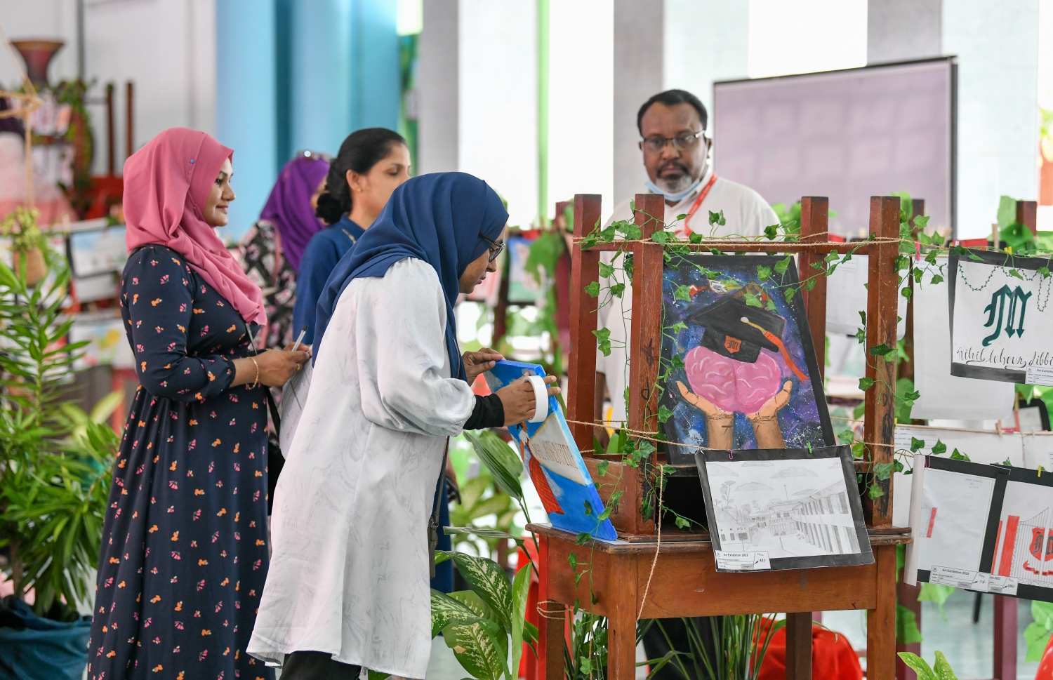 މަޖީދިއްޔާ ސްކޫލުގެ ކުދިންނާއި މުއައްޒަފުން، އެ ސްކޫލުގެ އަތްތެރި މަސައްކަތުގެ މައުރަޒަށް ހުށަހަޅާފައިވާ ބައެއް ކުރެހުންތައް އެ ސްކޫލުގެ ޓީޗަރުން ބަލަނީ.--- ފޮޓޯ: ފަޔާޒު މޫސާ | މިހާރު