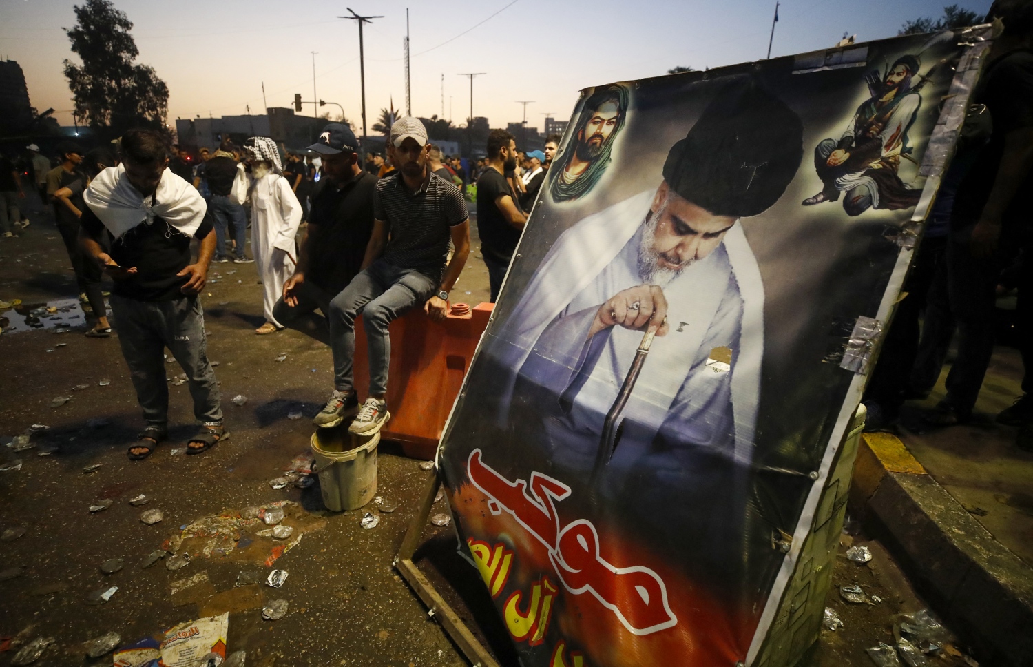 އޮގަސްޓް 29، 2022؛ އިރާގުގެ ވެރިރަށް ބަޣުދާދުގައި ހިނގަމުންދާ ހަމަނުޖެހުންތަކުގެ ތެރޭގައި، ނުފޫޒު ގަދަ ޝީއީ ލީޑަރު މުގްތަދާ އައް ސަދްރު އަށް ތާއީދުކުރާ ބަޔަކު އޭނާގެ ފޮޓޯތައް ހިފައިގެން ސަރުކާރާ ދެކޮޅަށް އަޑު އުފުލަނީ. --އޭއެފްޕީ