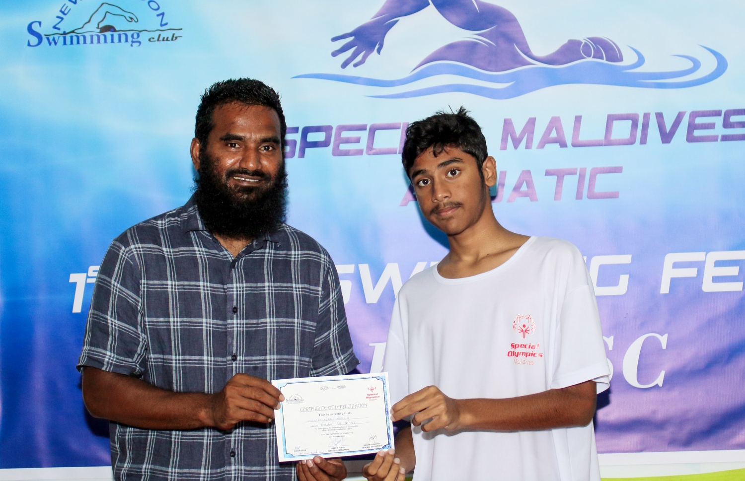 ނިއު ލެގޫންގެ ފަރާތުން ހުޅުމާލޭގެ ސްވިމިން ޕޫލްގައި ބޭއްވި ސްޕެޝަލް އޮލިމްޕިކްގައި ބައިވެރިވި ކުއްޖަކަށް ދިވެހި ގައުމީ ފުޓުބޯޅަ ޓީމުގެ ކެޕްޓަން އަލީ އަޝްފާގު (ދަގަނޑޭ) ސެޓްފިކެޓް ހަވާލުކުރަނީ.--- ފޮޓޯ: ނިއު ލެގޫން ސްވިމިން ކްލަބް