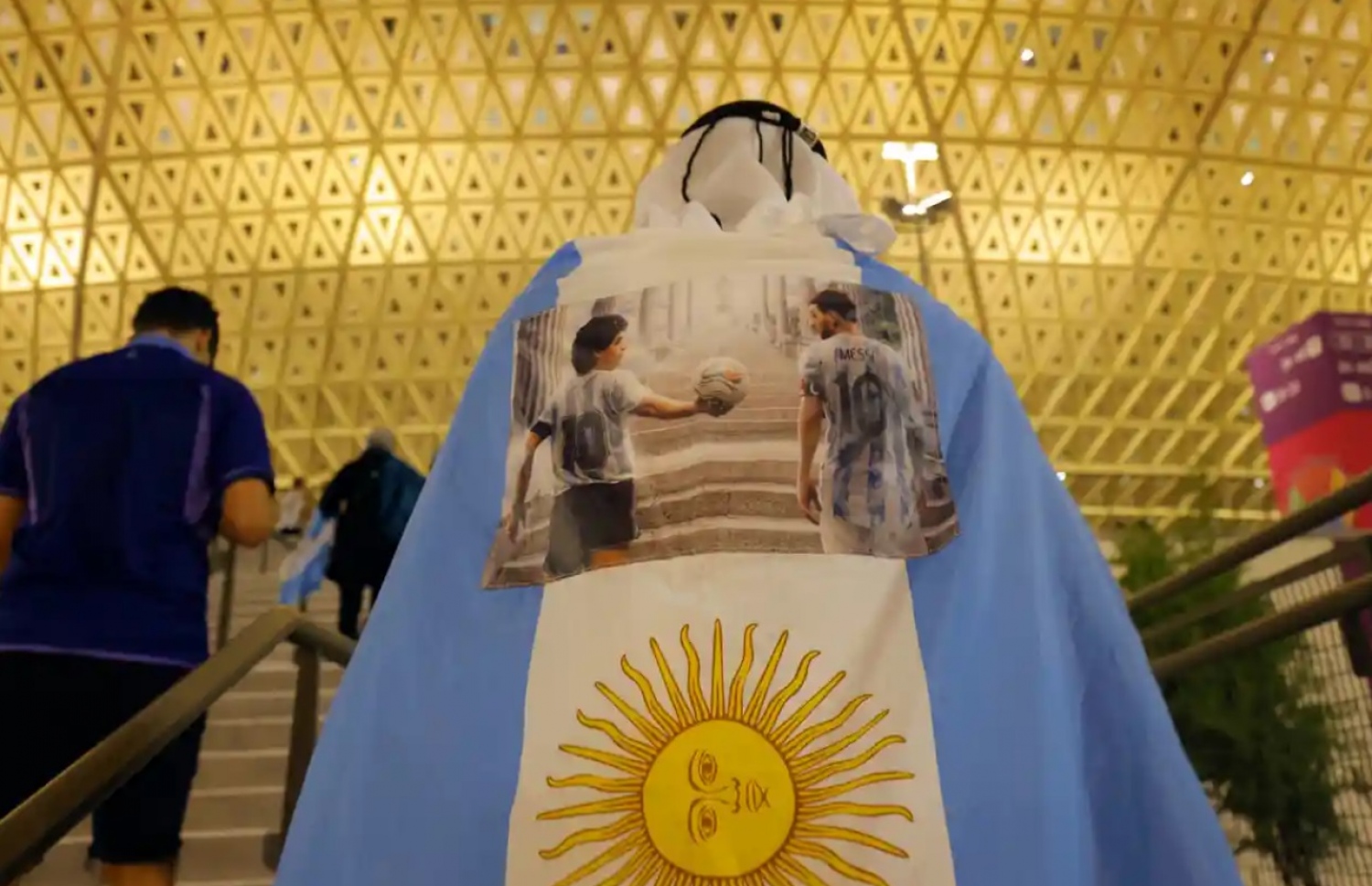 ލުސައިލްގެ އައިކޮނިކް ސްޓޭޑިއަމް ކައިރީގައި އާޖެންޓީނާގެ ސަޕޯޓަރަކު އެ ގައުމުގެ ދިދަ ހިފައިގެން: އެ ދިދައިގައި މެސީ އާއި މެރަޑޯނާގެ ފޮޓޯއެއް ހަރުކޮށްފައި.