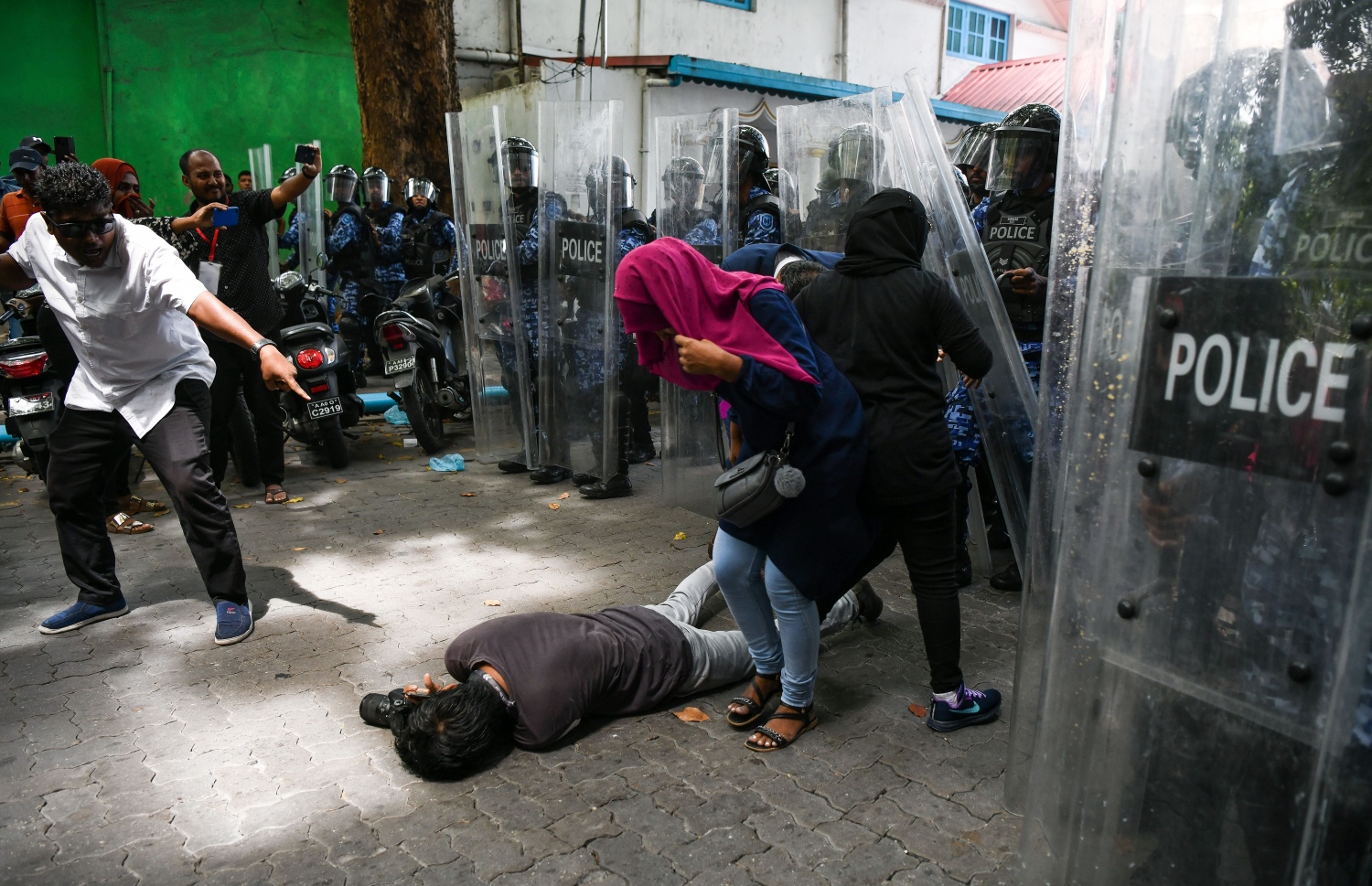 ޝީލްޑުތަކާ އެކު ތިބި ފުލުހުންގެ ސަފު ކުރިއަށް ޖެހުނު ވަގުތު ފުލުހުންގެ ކައިރީގައި ހުރި ޗެނަލް 13ގެ ނޫސްވެރިއަކަށް އަނިޔާވެ، މަގުމައްޗަށް ވެއްޓިފައި.--- ފޮޓޯ: ފަޔާޒު މޫސާ | މިހާރު